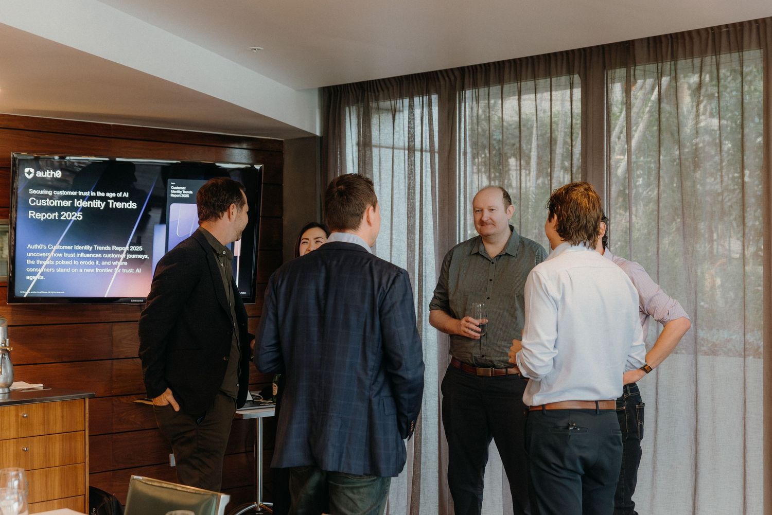 A group of business professionals having a discussion in front of a TV screen in a modern office setting.