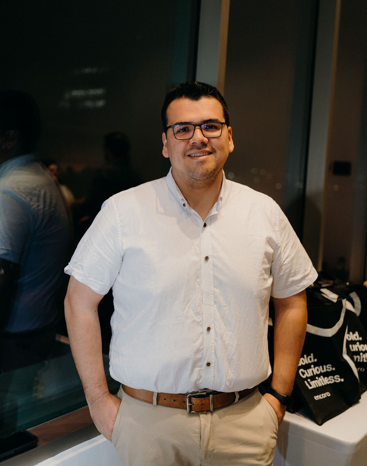 A person in a white button-down shirt and glasses stands indoors with a slight smile in a series of similar poses.