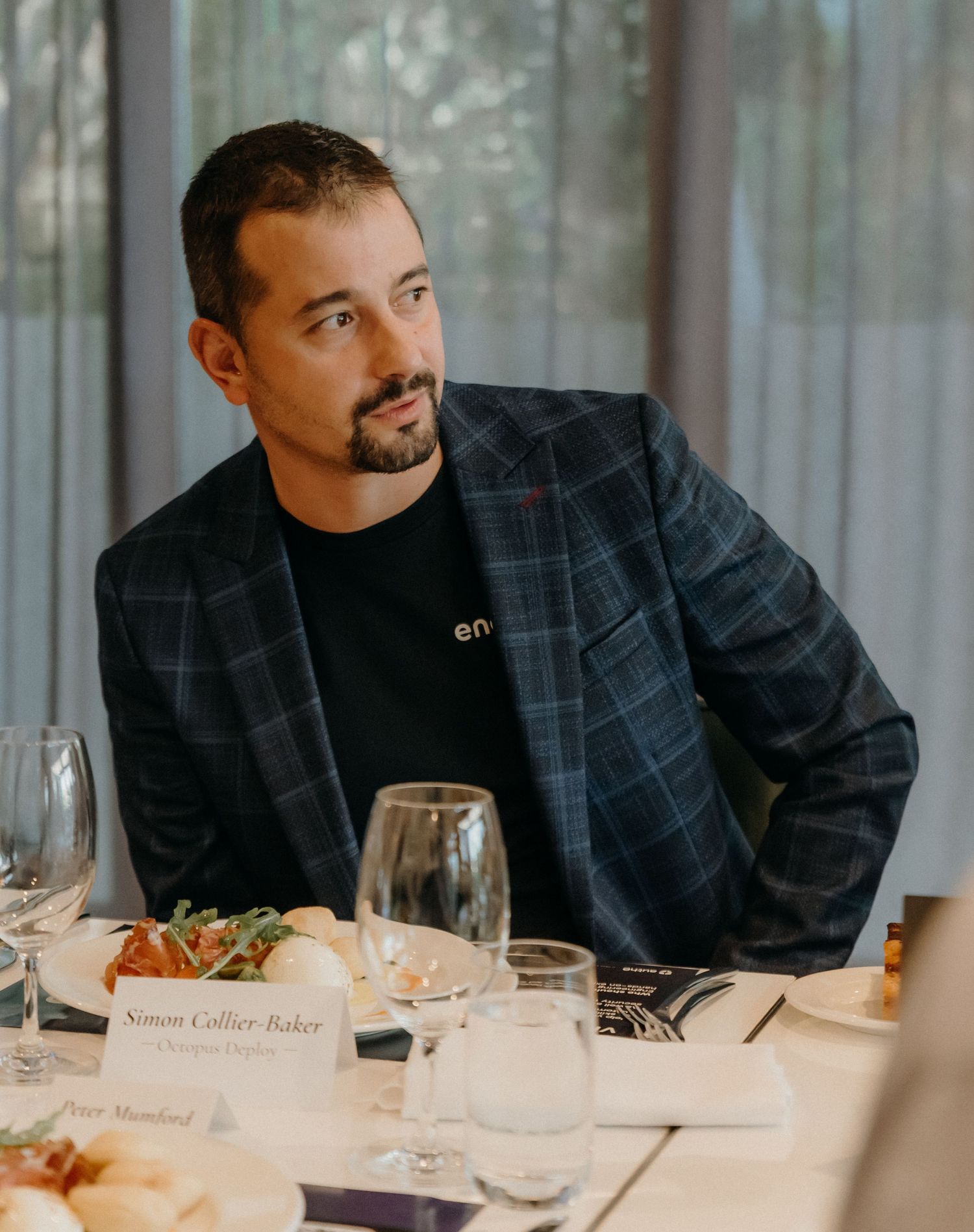Professional diner wearing a dark plaid blazer and black shirt sits at an elegant table setting with wine glasses.