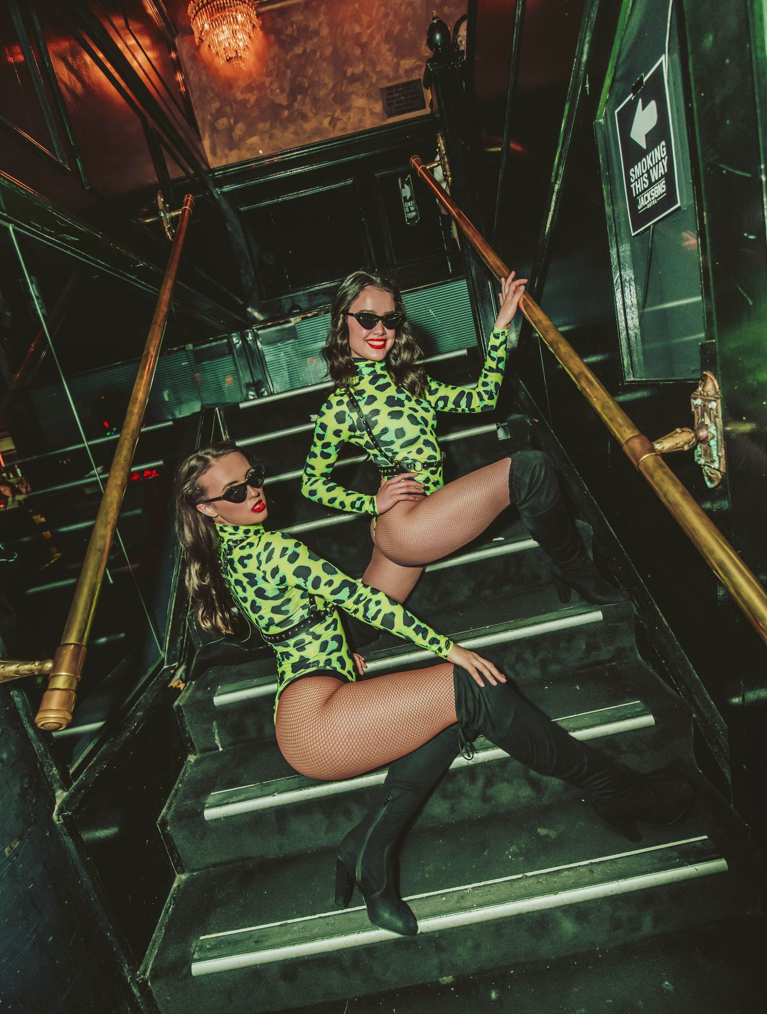 Dancer in neon green patterned bodysuit performs dynamic poses on illuminated steps in dark nightclub setting.