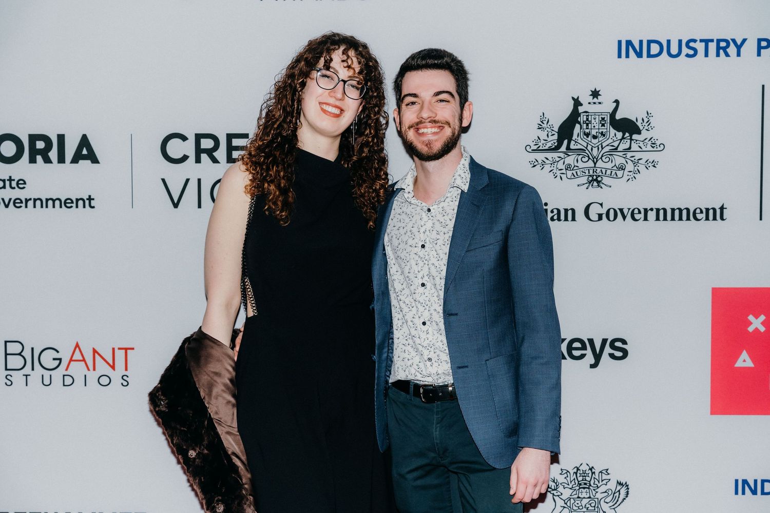 People in formal attire pose together at an industry event with sponsor banners and logos visible in the background.