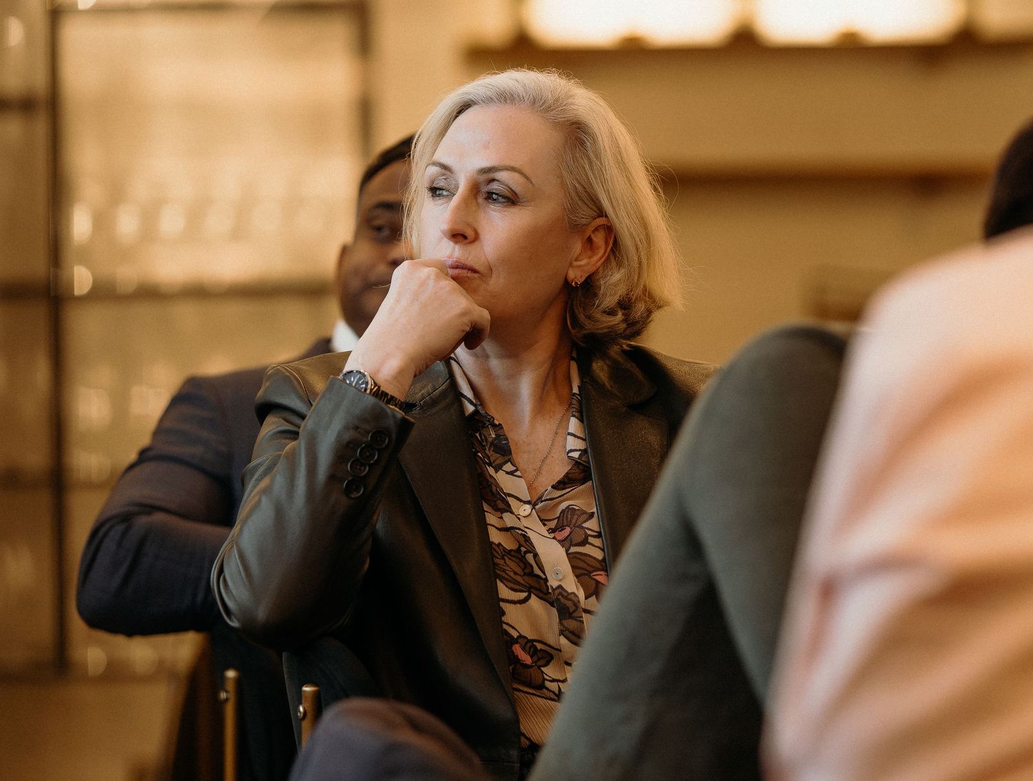 A person with blonde hair in a black outfit sits at a dimly lit restaurant table.