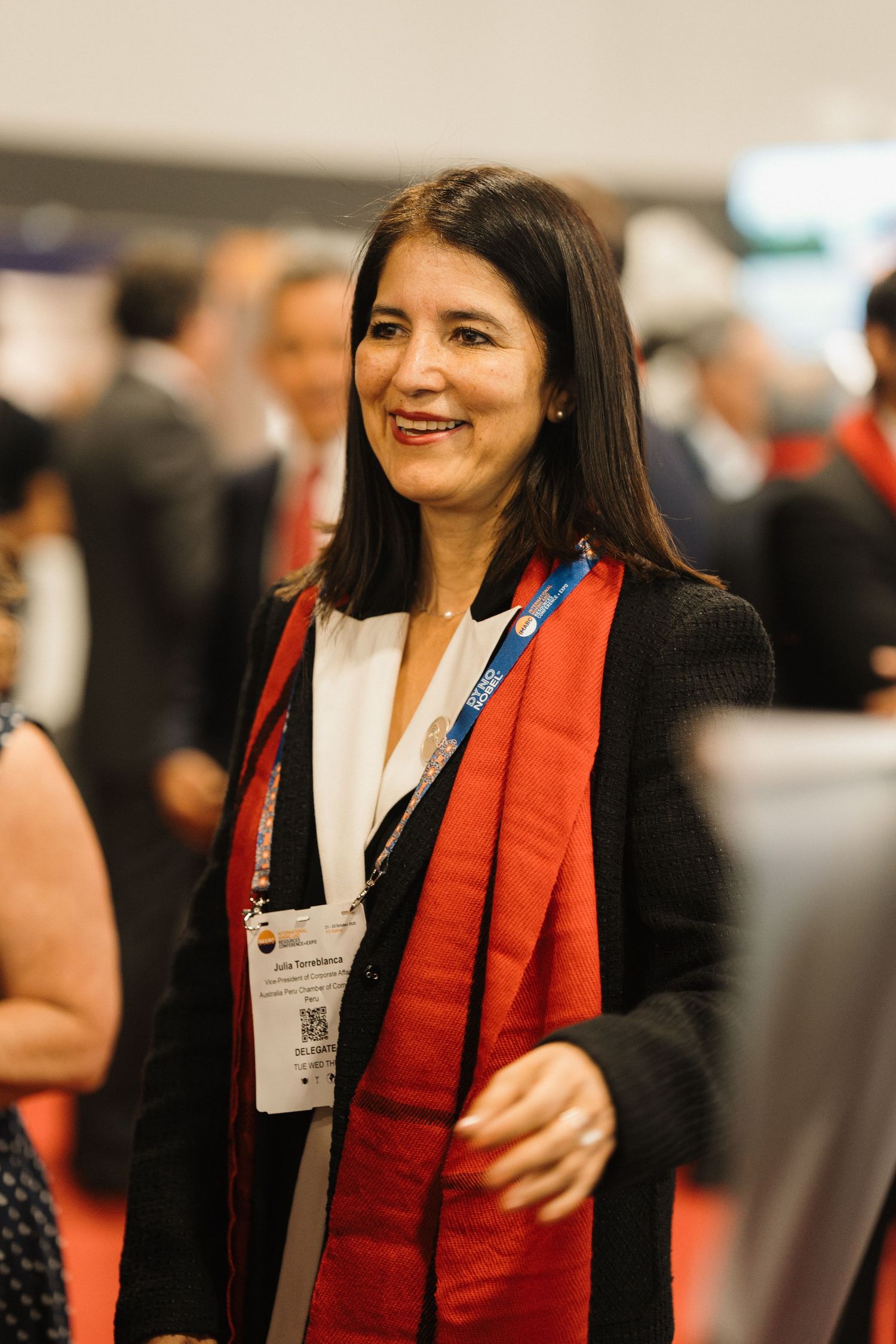 A person in business attire wearing a red scarf smiles warmly at a professional event.