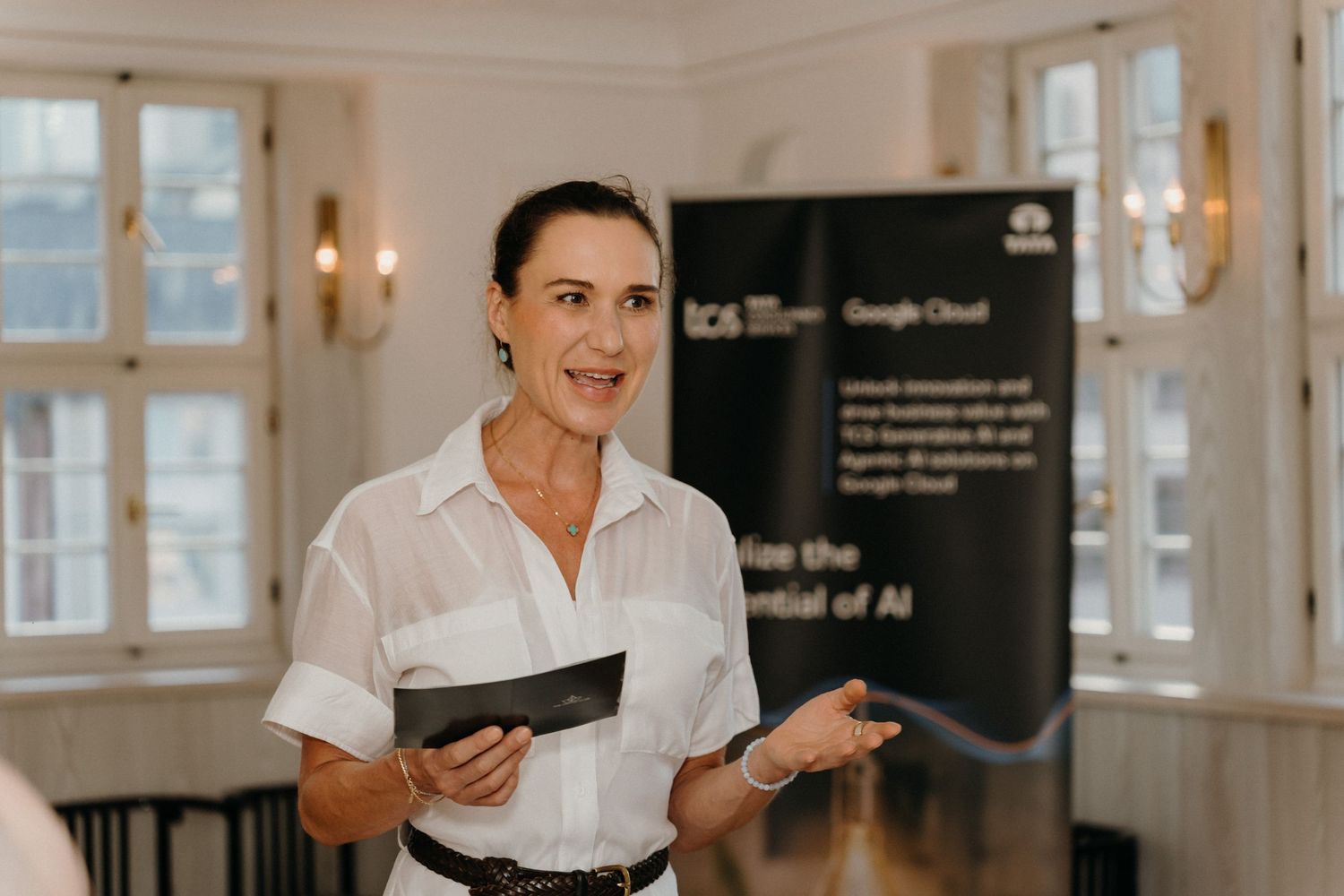 Woman presenting at Google Cloud TCS event, holding tablet, gesturing confidently in elegant venue.