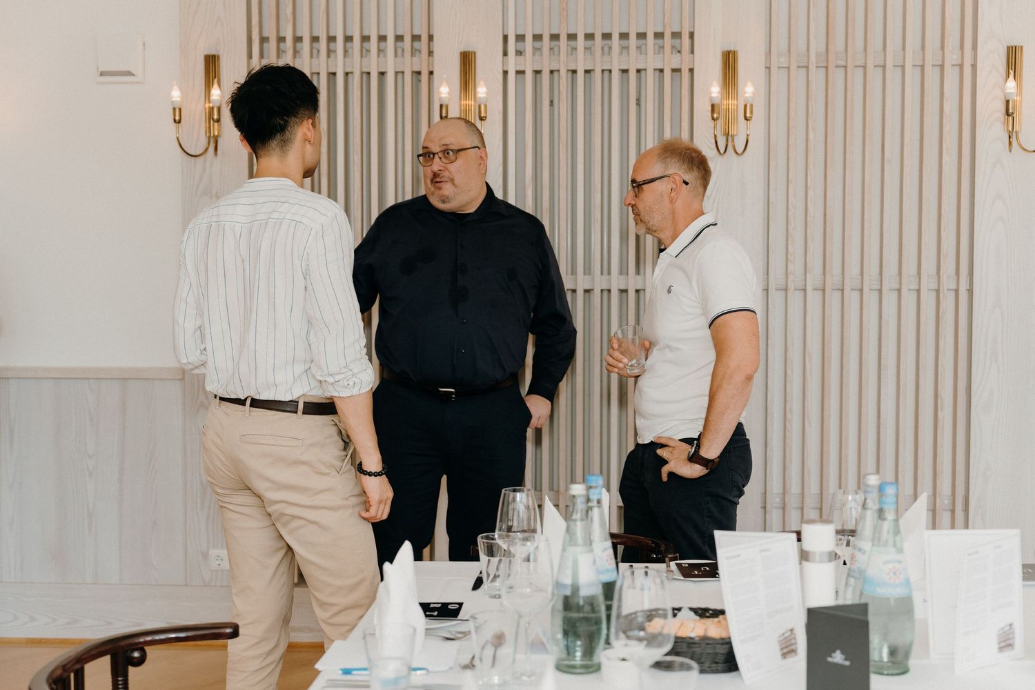 Three businessmen engaged in conversation at an elegant indoor networking event with a formal table setting.