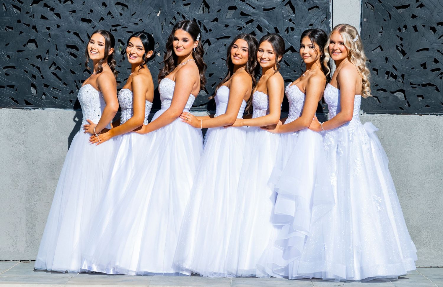 A group of bridesmaids in white dresses stands in line for a coordinated wedding party photo.