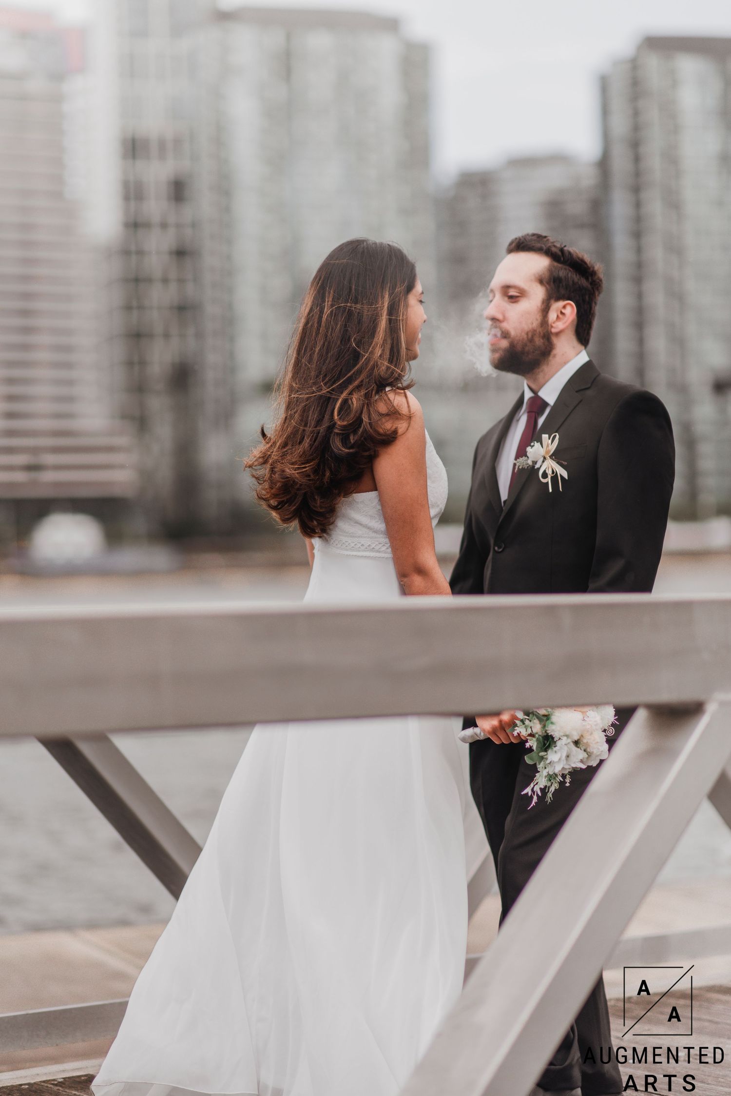 A couple shares an intimate moment on a rooftop terrace with urban high-rise buildings in the background.