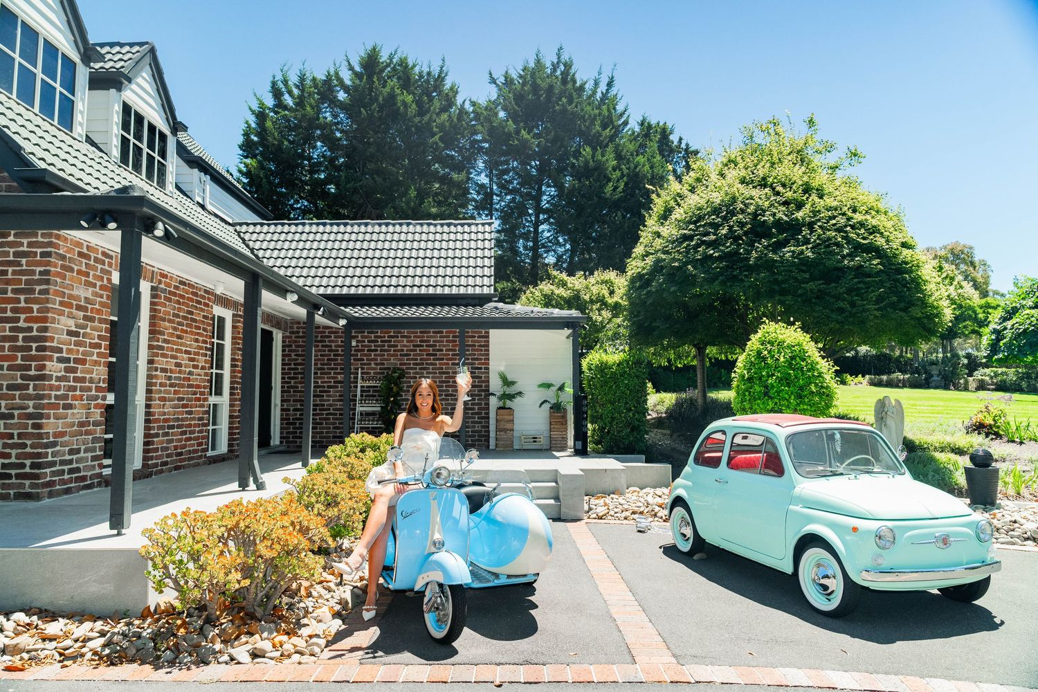 Several mint-colored vintage cars are parked near brick buildings and lush green foliage.