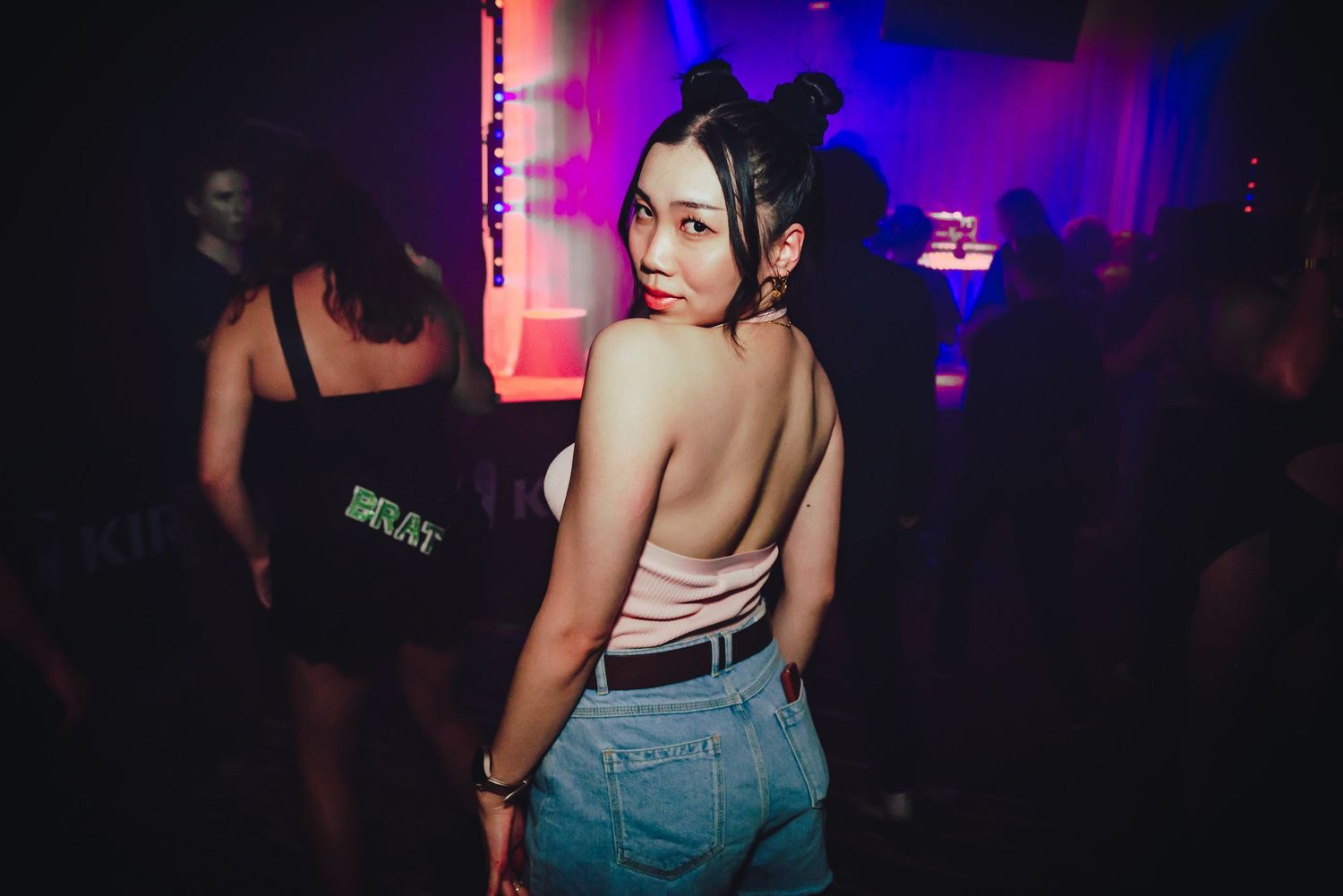 People dancing and socializing in a dimly lit nightclub with purple and red lighting effects.