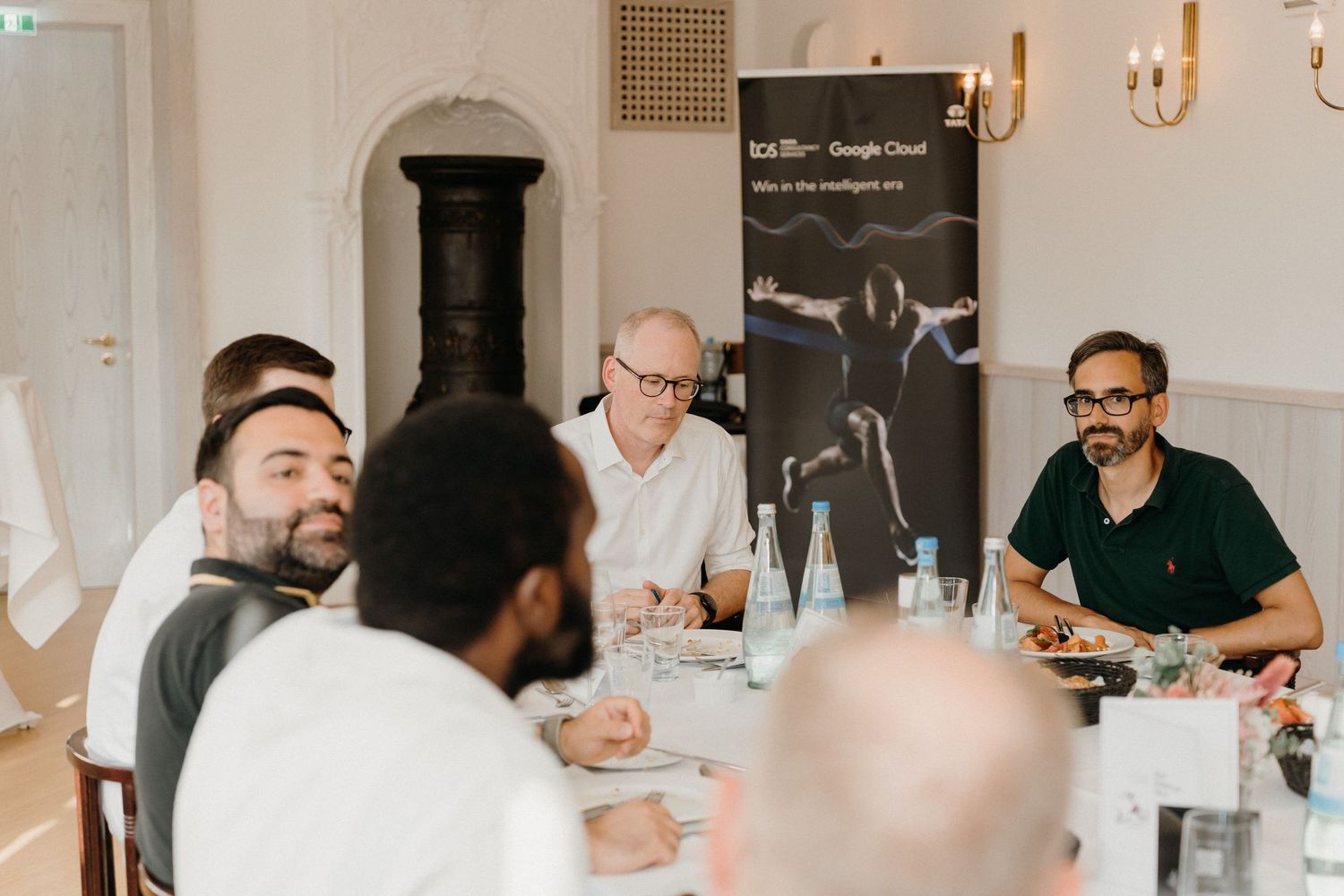 Business professionals engaged in discussion at a corporate dinner event with a Google Cloud banner visible in the background.