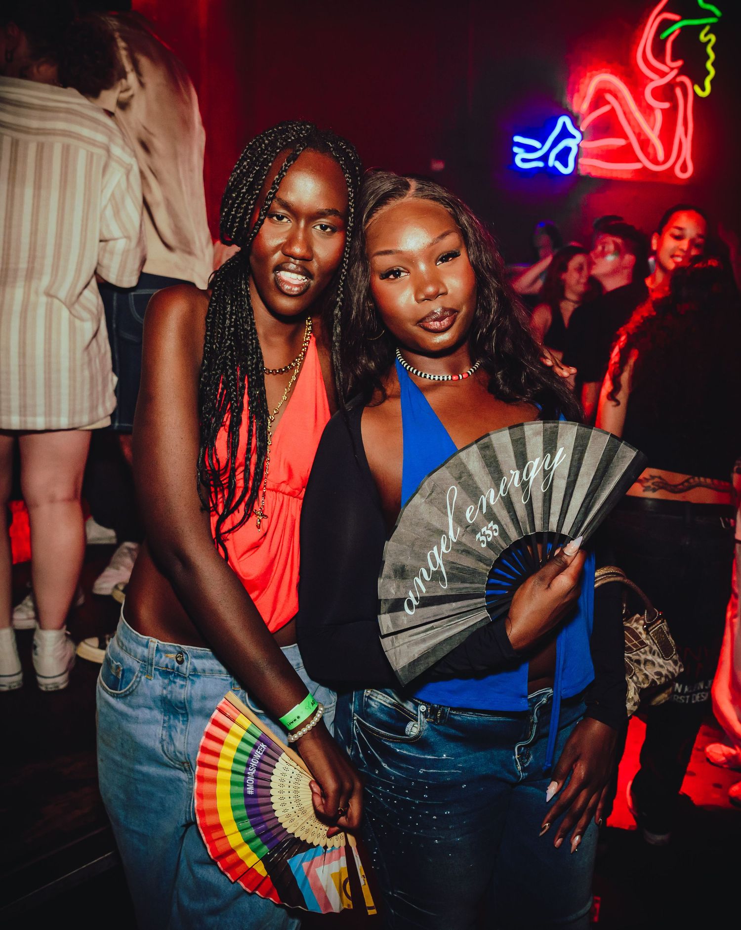 Group of friends dancing and posing with decorative fans at a nightclub with neon lights in the background.