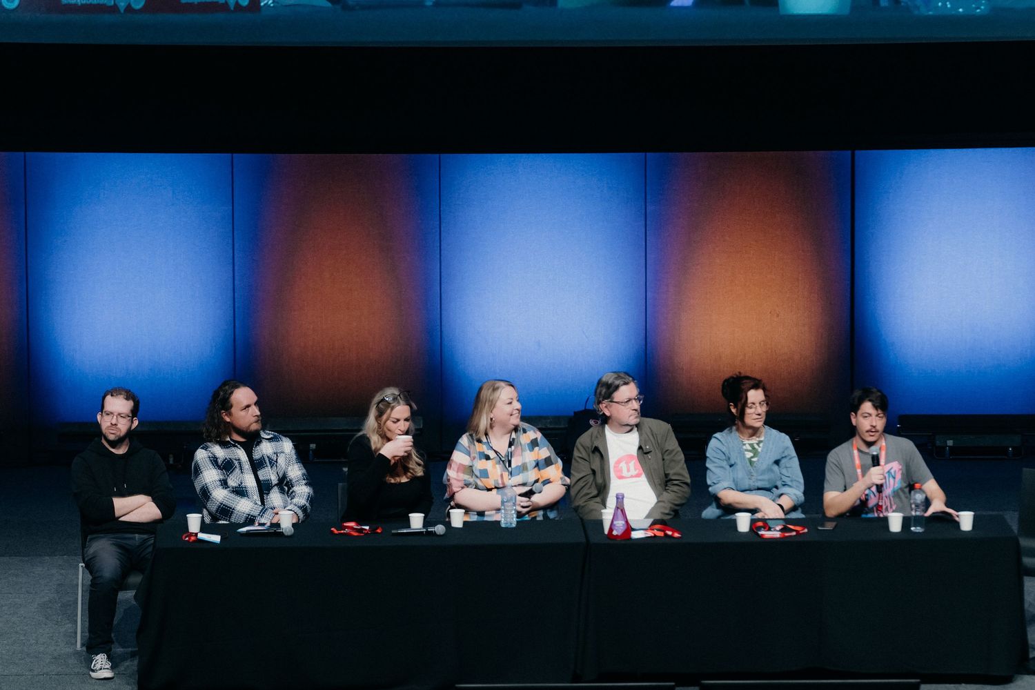 People sitting at a long panel table on stage during a conference or event presentation.