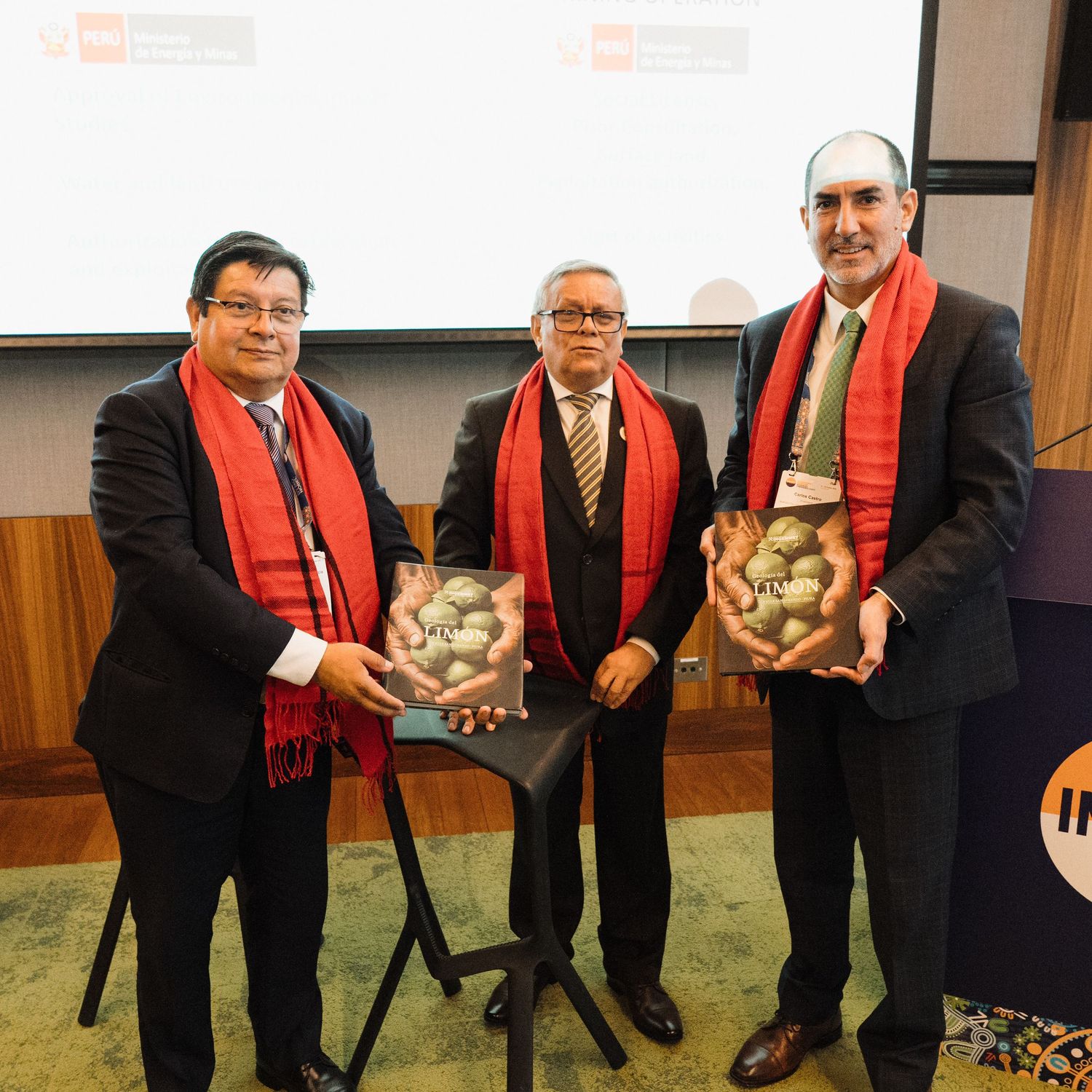 A group wearing red scarves and dark clothing poses together holding small decorative objects in an indoor setting.