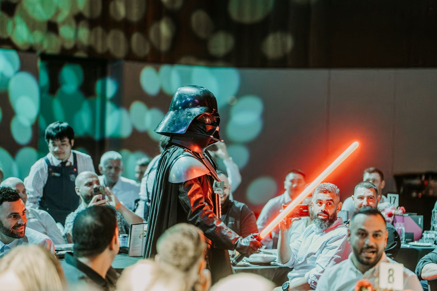 A group of performers on stage hold glowing red lightsabers during a Star Wars themed entertainment show.
