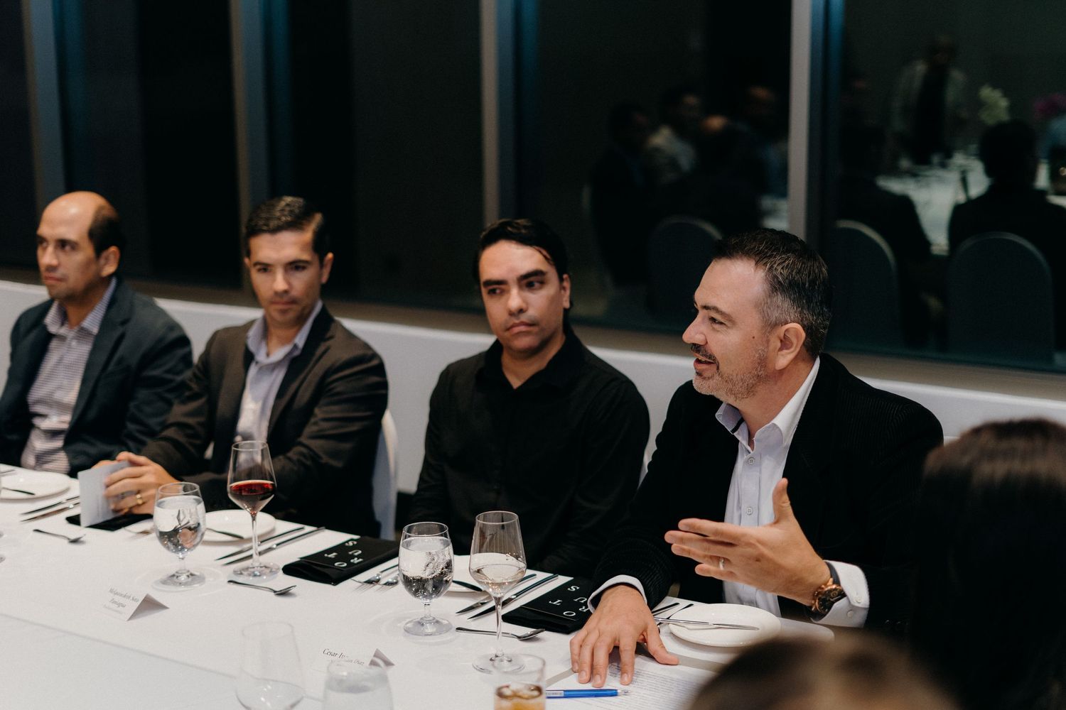 Business professionals engage in discussion around a long conference table during a corporate dinner meeting.