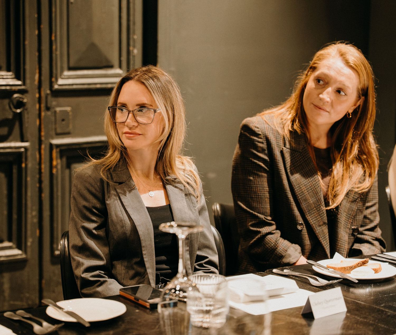 Business professionals seated at a conference table during a meeting with plates and water glasses.
