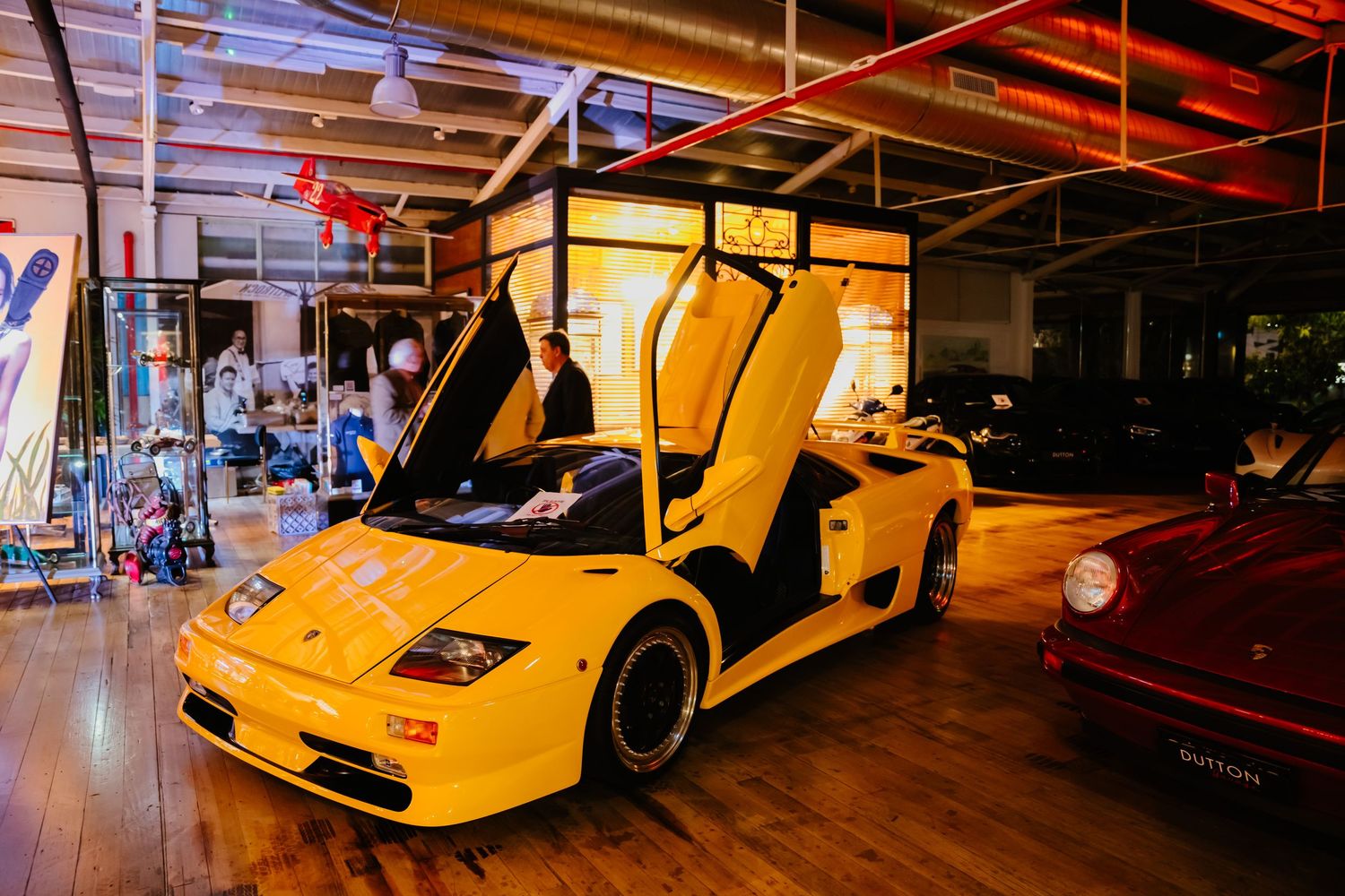 Yellow Lamborghini Diablo supercar displayed in red-lit showroom with striking scissor doors open and dramatic lighting.