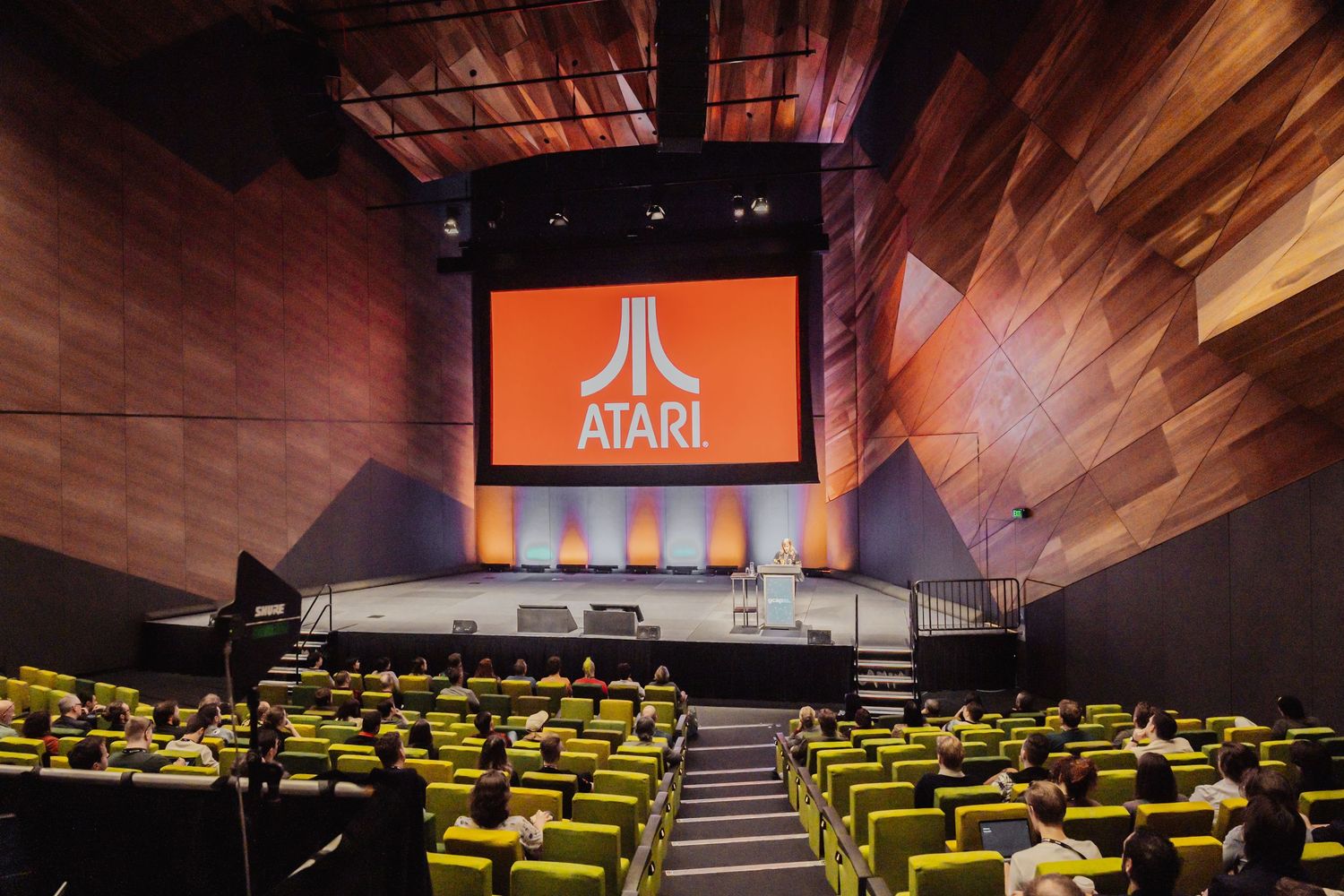 Movie theater interior with rows of bright yellow seating and wood paneled walls featuring an Atari logo display.