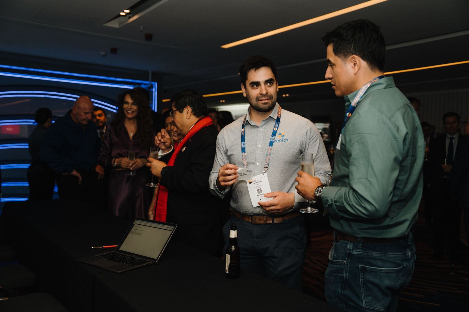 People networking and having discussions in a dimly lit conference or event space with blue lighting accents.