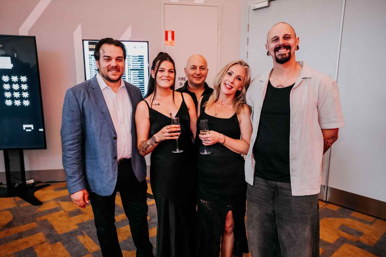 A group of people in formal attire pose together at a social gathering in an indoor venue.