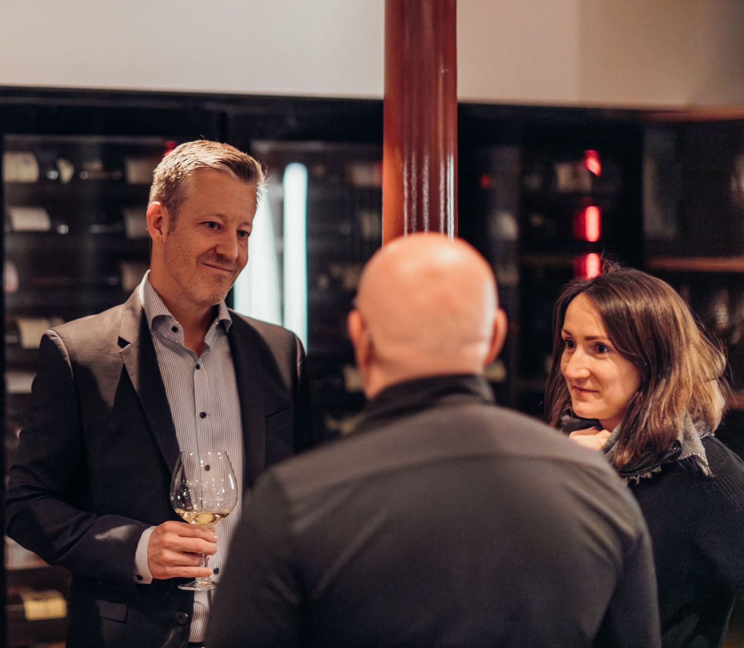 Business professionals networking and socializing at an upscale evening event with wine glasses in hand.