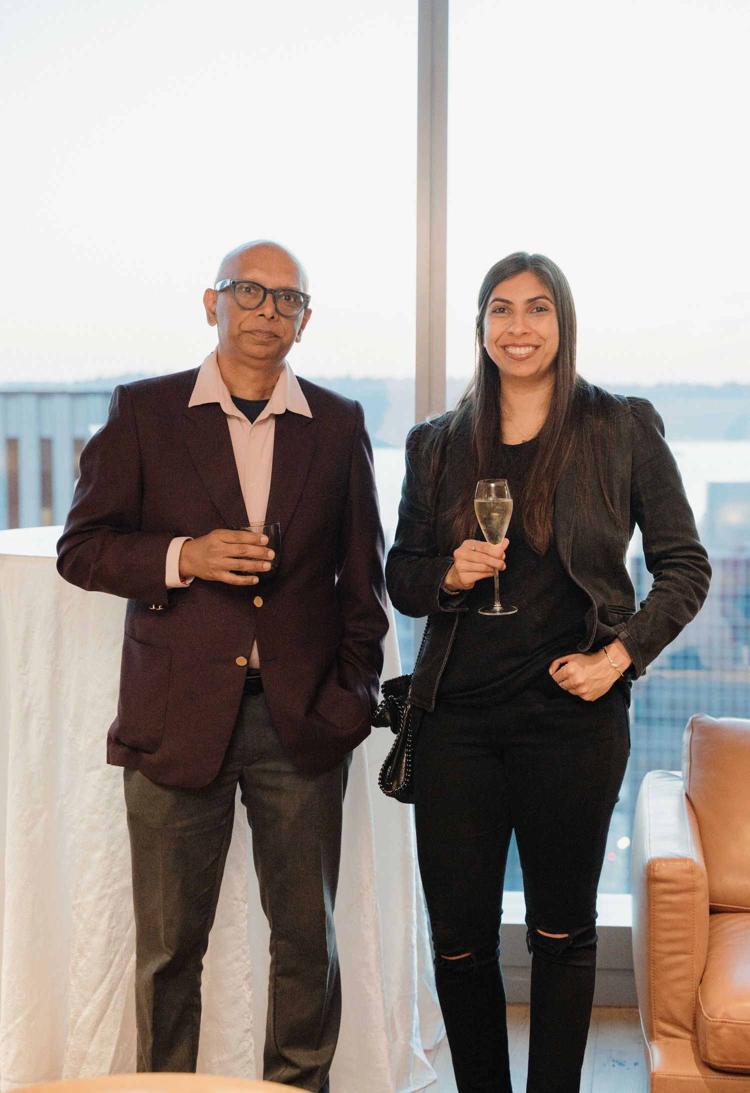 Business professionals in dark attire holding champagne glasses stand together in a modern office space with city views.