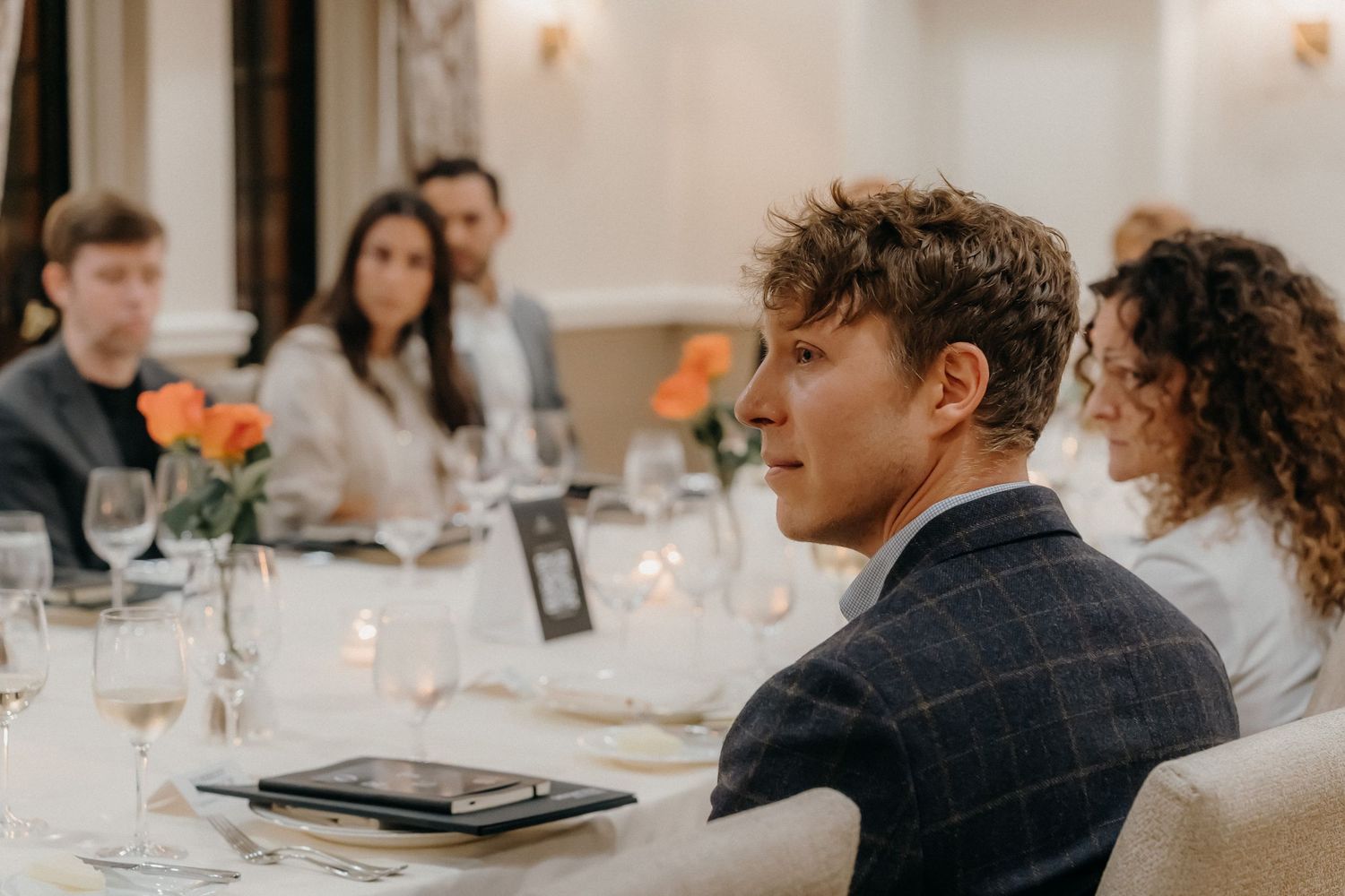 People gathered around an elegant dining table with orange flowers and glassware at an upscale restaurant setting.