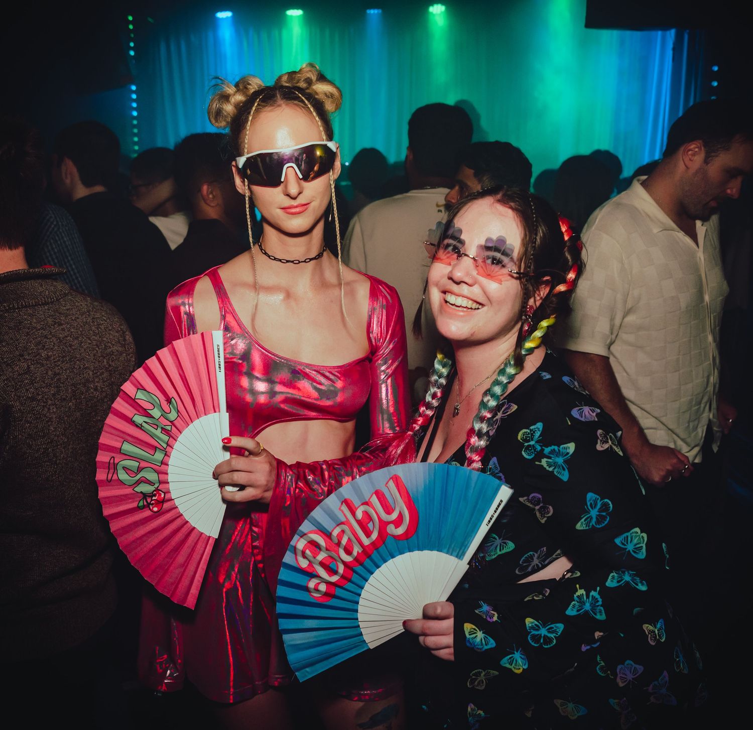 Nightclub scene with colorful green and blue lighting showing people dancing and holding decorative hand fans.
