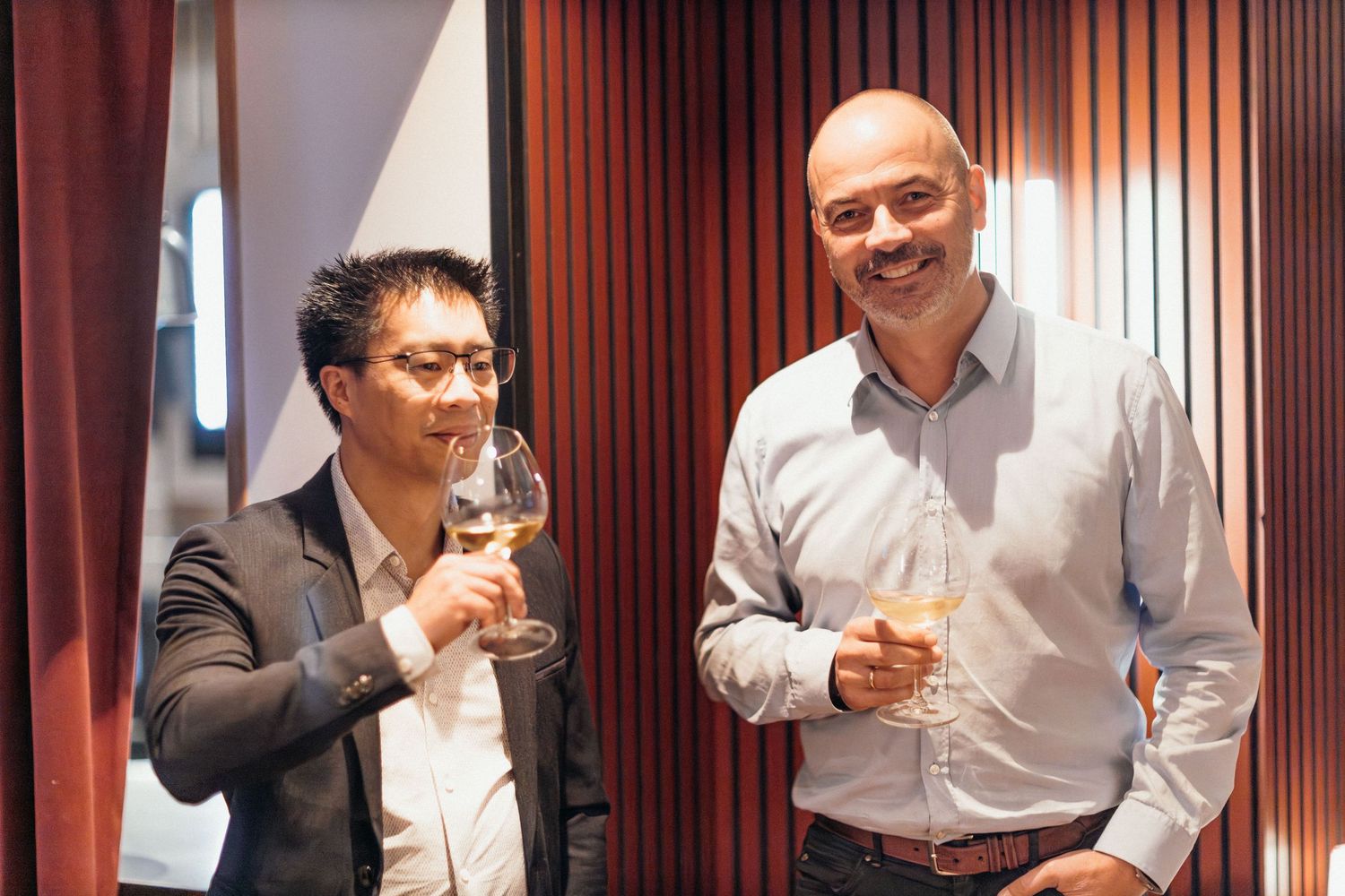 People in white and dark business attire enjoying drinks and conversation at a social gathering.