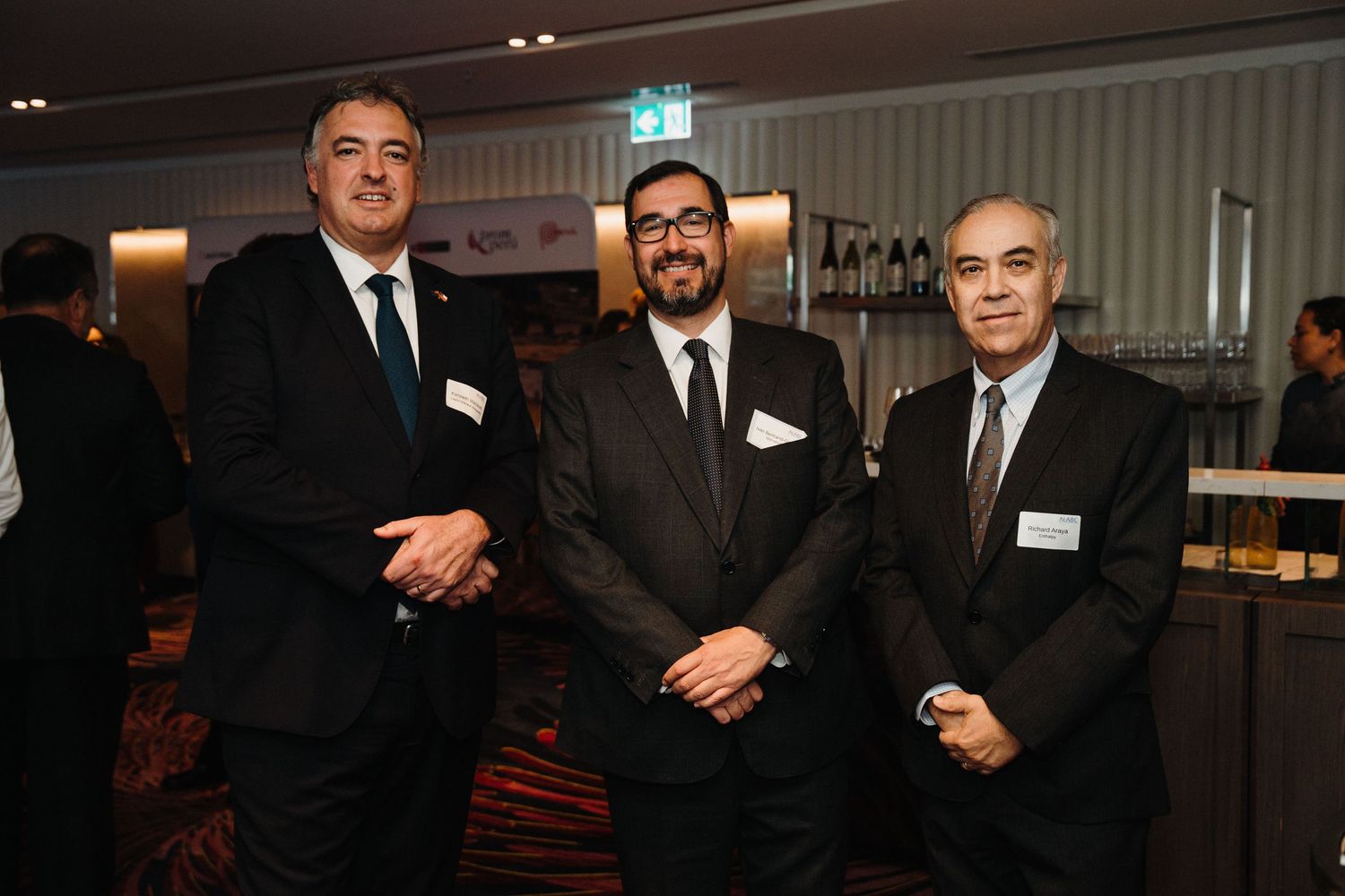 Three businessmen in dark suits pose together at a formal networking event.