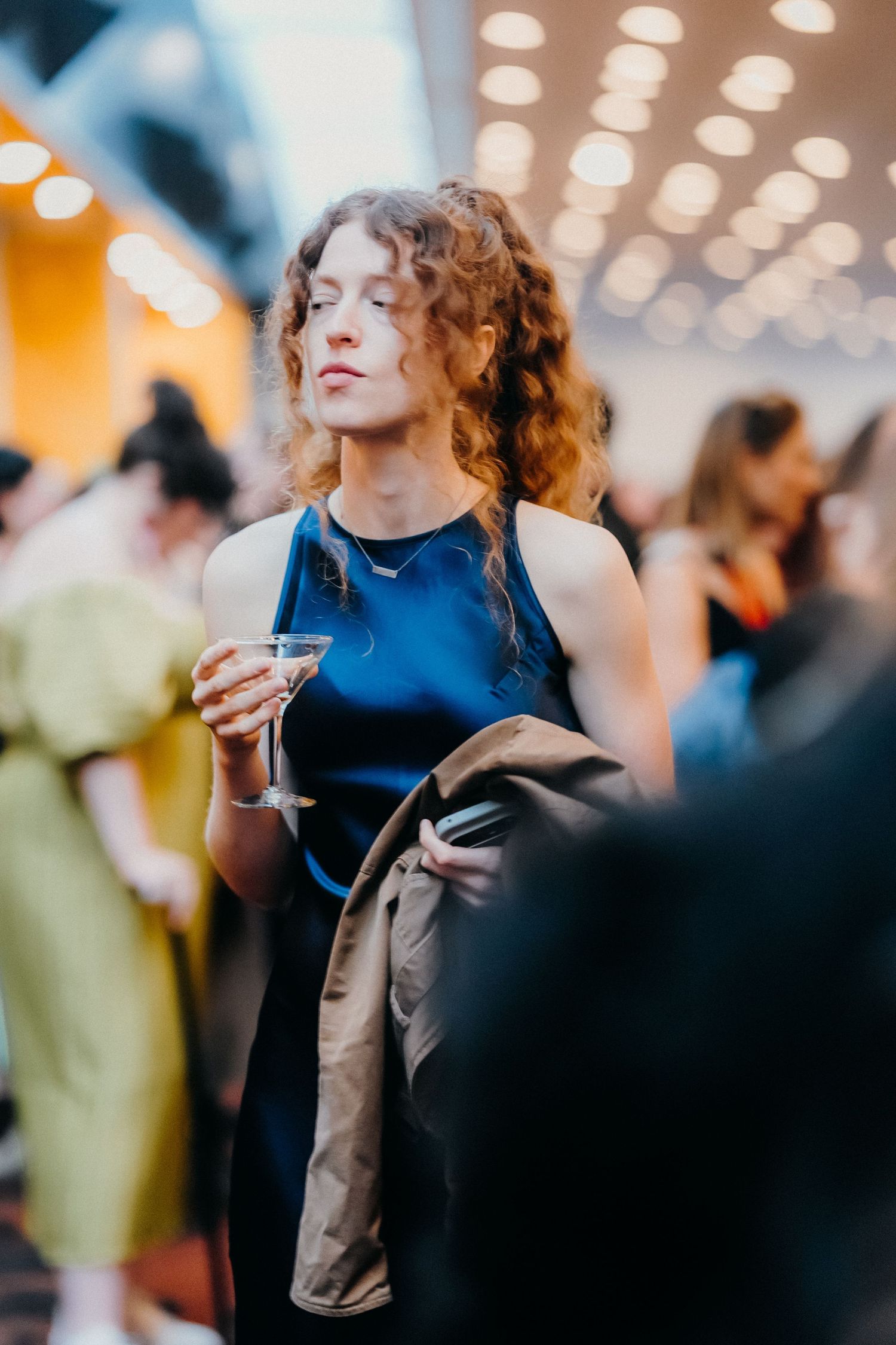 A person in a navy blue top with curly hair dances gracefully under warm lighting at an indoor event.