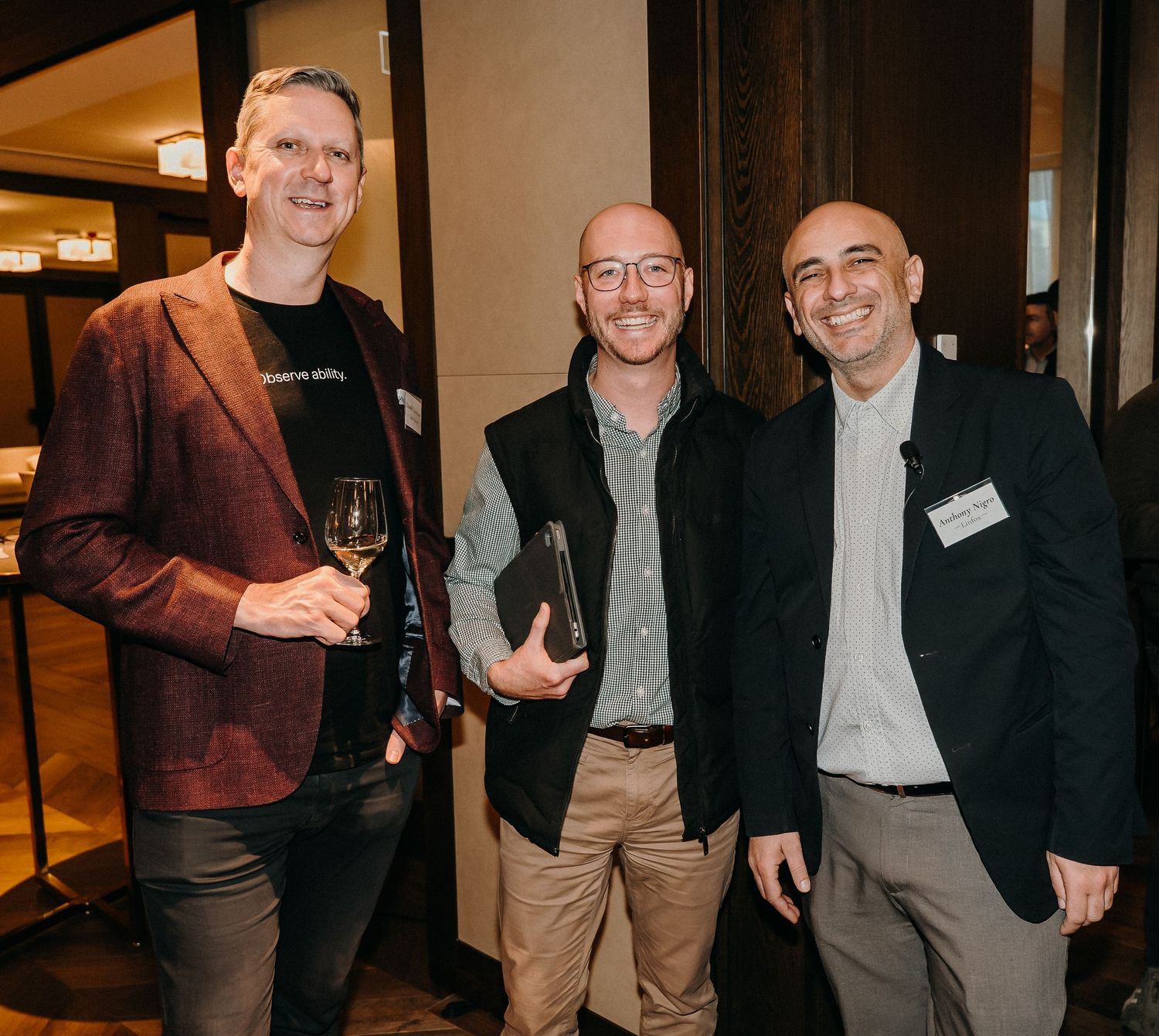 Three people in business attire stand together smiling at a professional networking event.