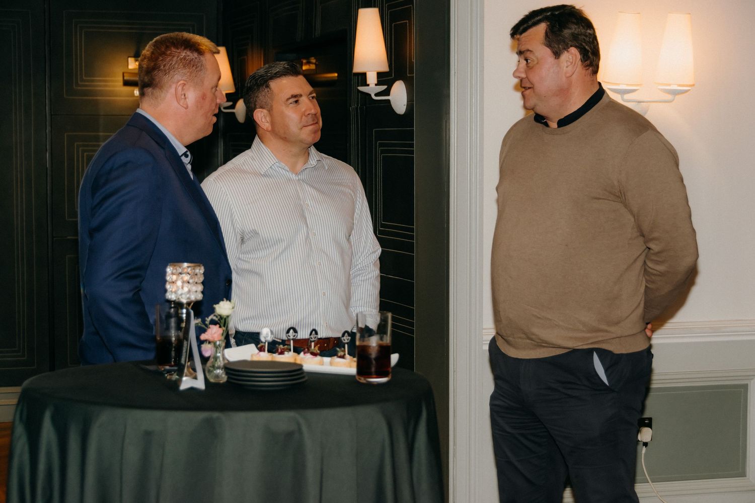Group of people engaged in conversation at an indoor business gathering or networking event.