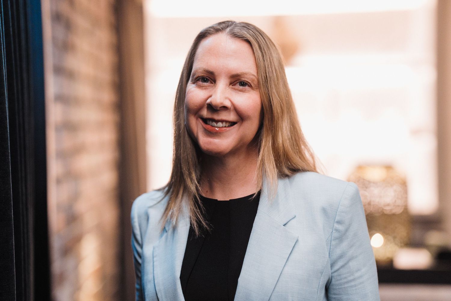 Professional headshot photos of someone wearing a light blue blazer and black top against a warm-toned background.
