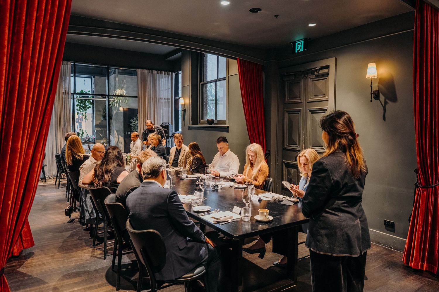 Diners seated at a long table with red curtains in an upscale restaurant's intimate dining space.