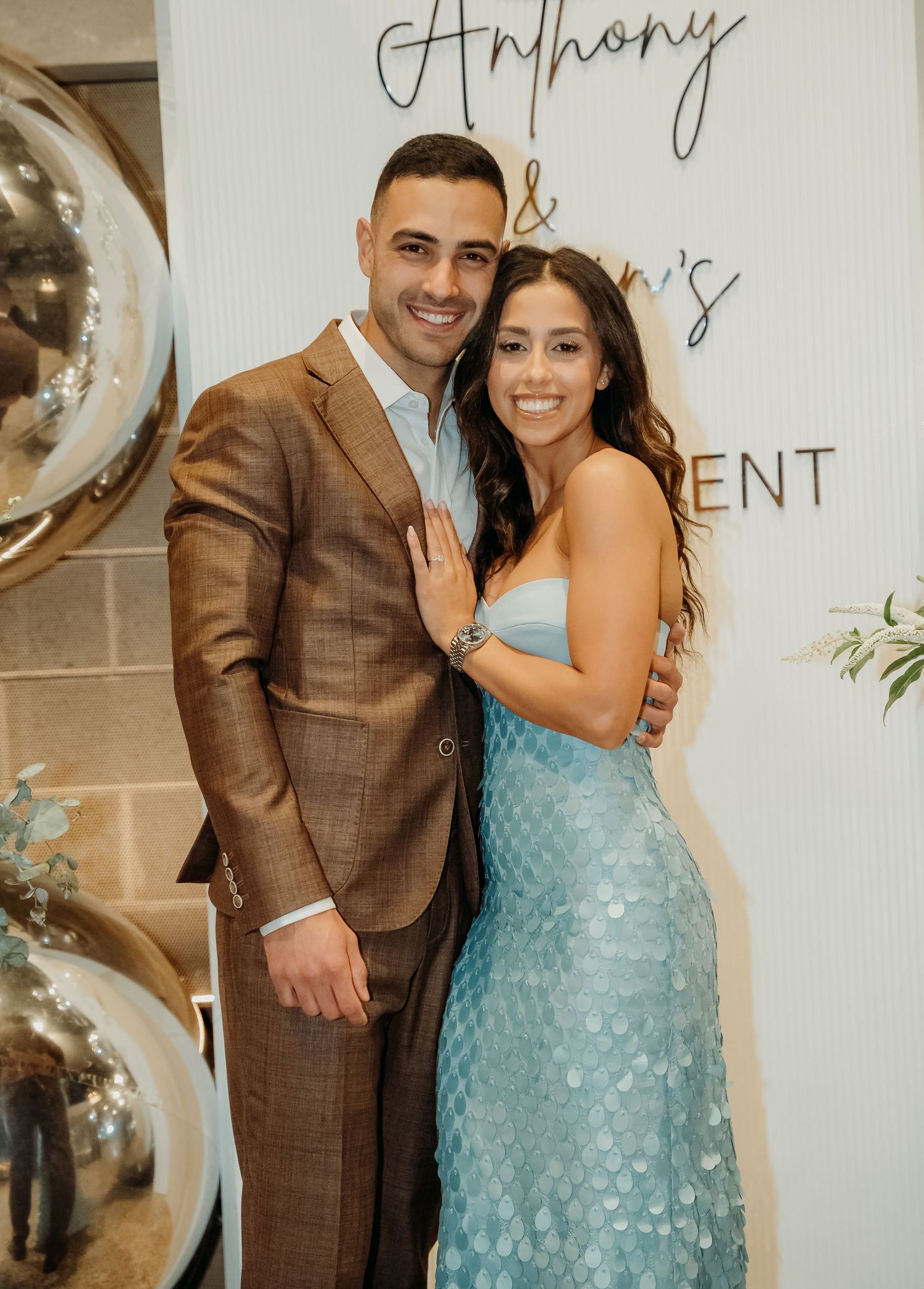 A couple poses together in a joyful engagement photo session, with the woman wearing a sparkly blue dress.