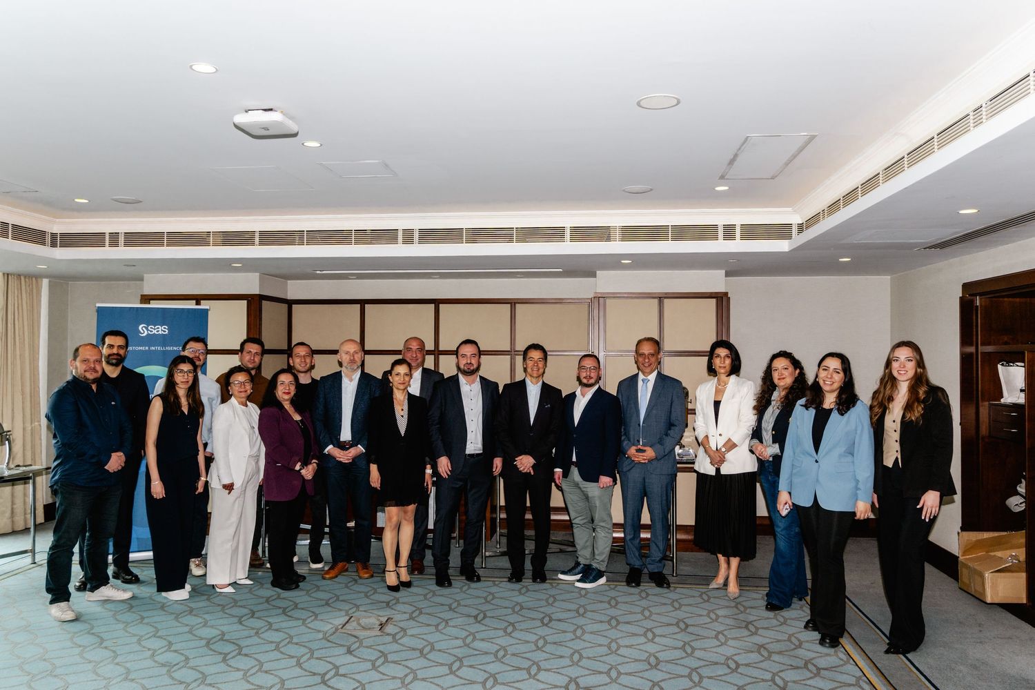 Group of business professionals posing together in a modern conference room near a branded banner.