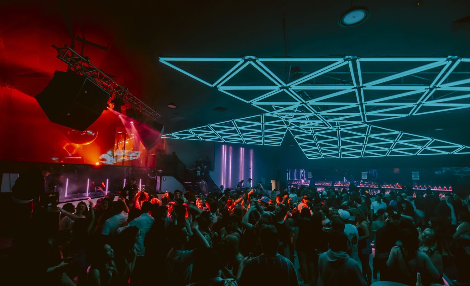 Concert crowd dances under geometric neon blue lighting at an electronic music festival.