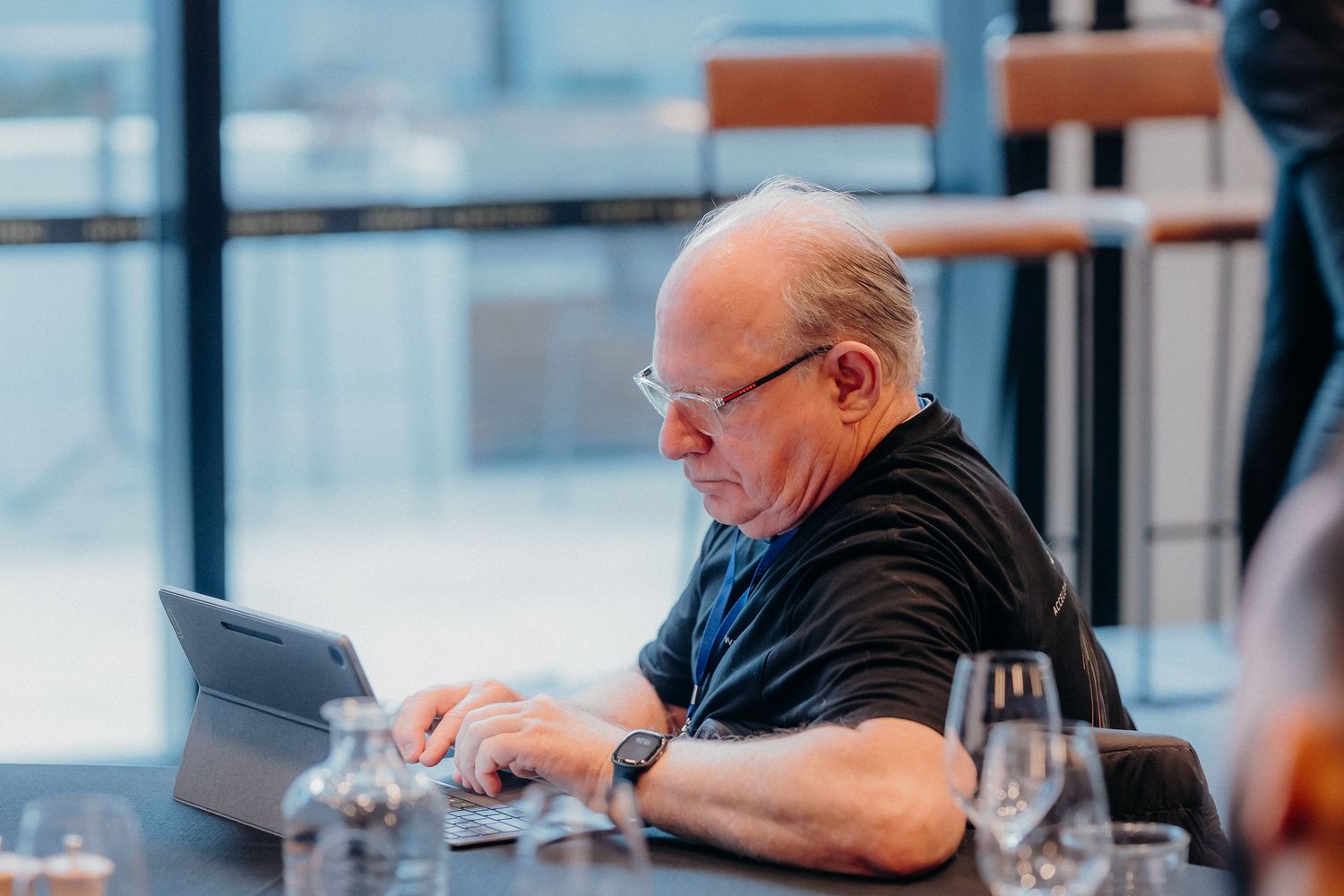 A person in a black shirt sits at a table working on a laptop computer in a bright modern space.
