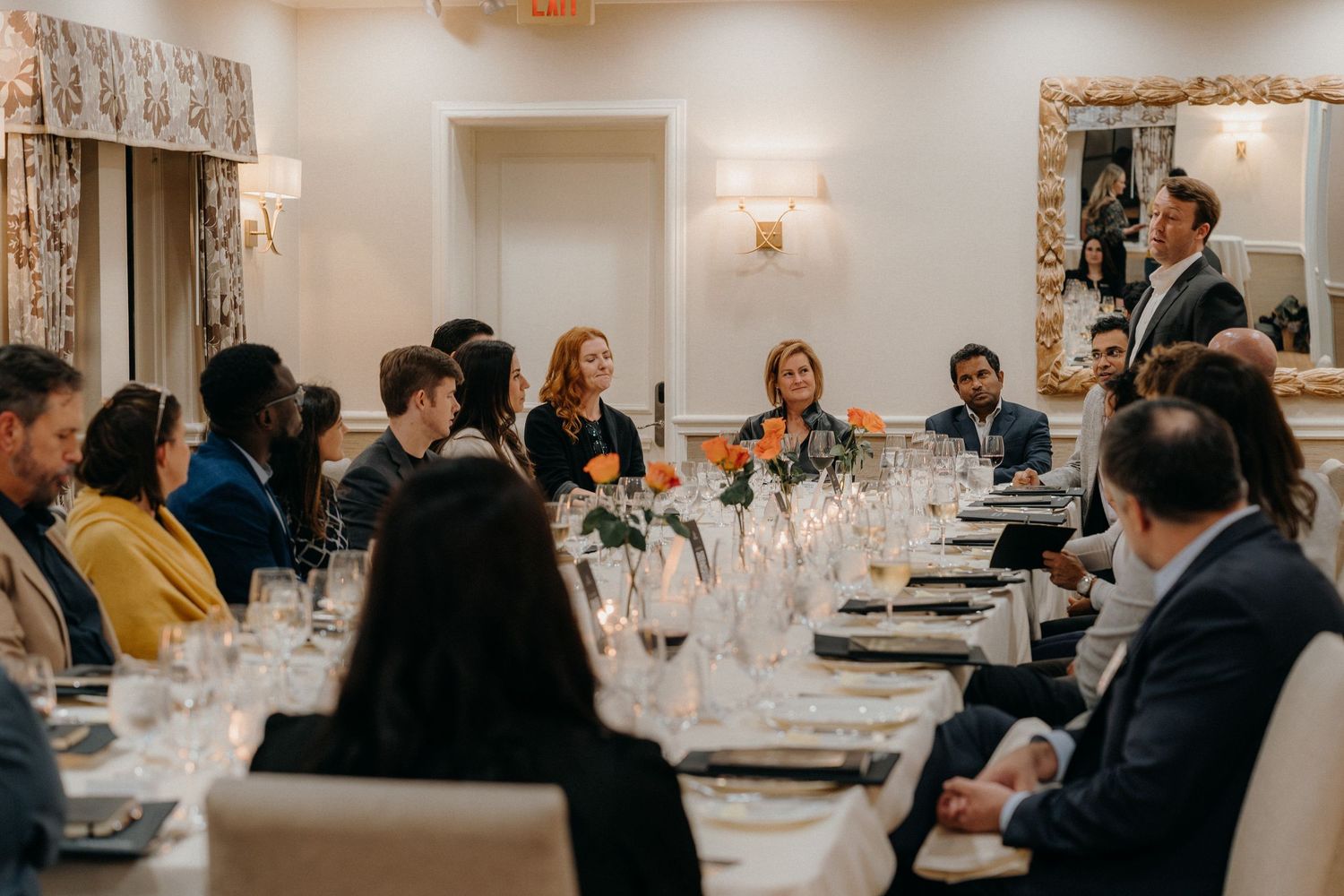 A panoramic view of a formal dining event with guests seated at long tables in an elegant room with wall sconces.