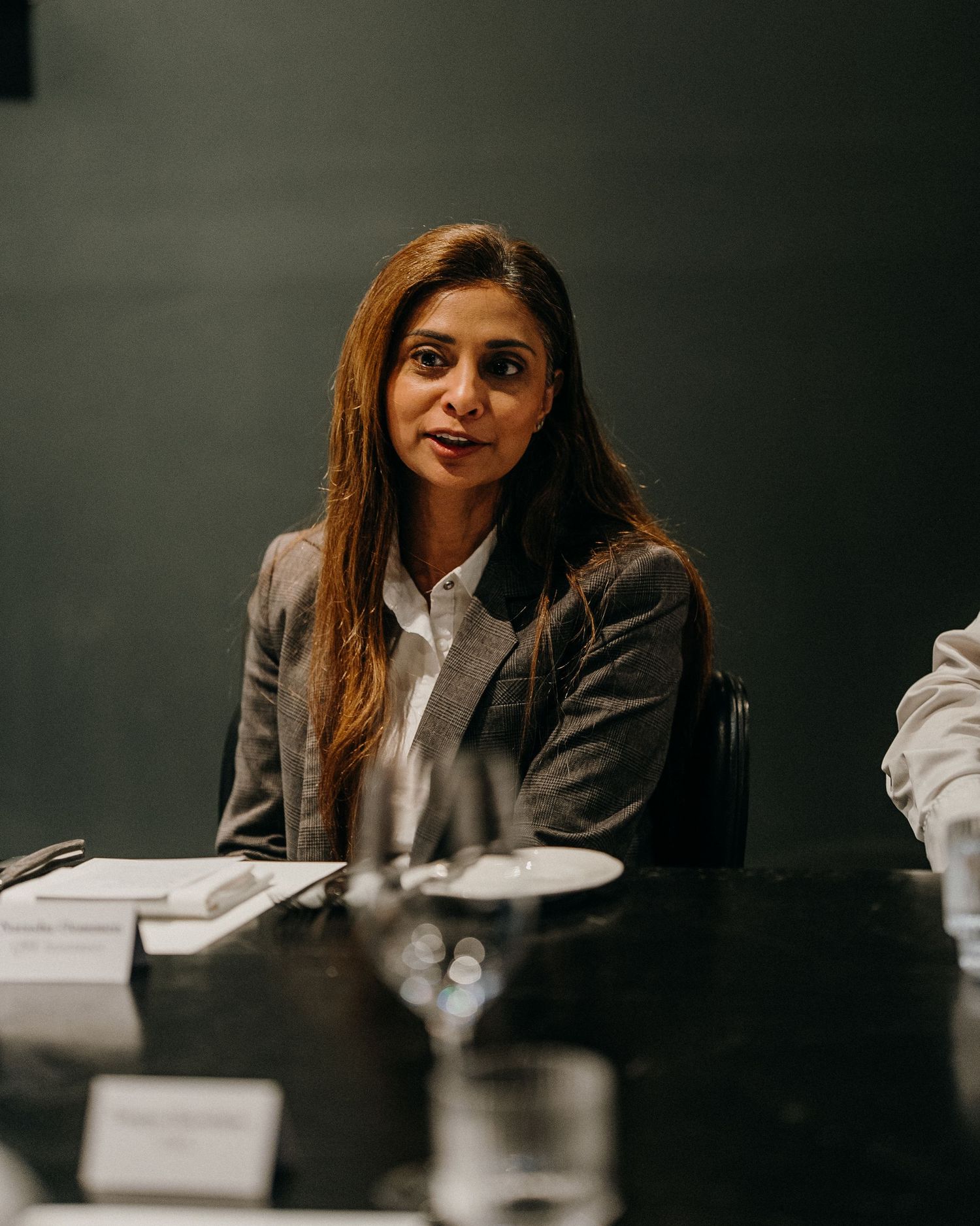 Professional in a gray blazer and white shirt sits attentively at a conference table during a business meeting.