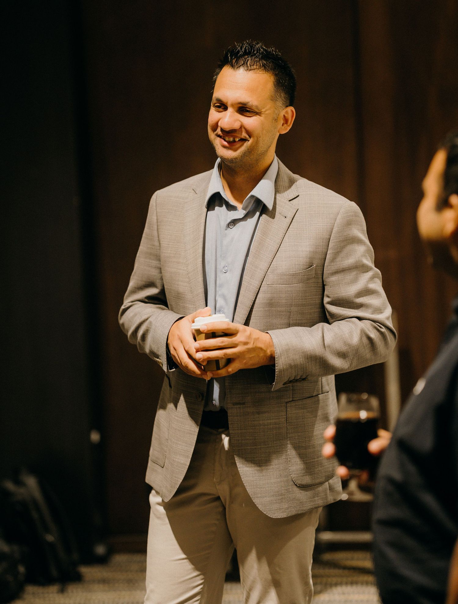 Smiling man in a beige suit holding a drink at a formal networking event.