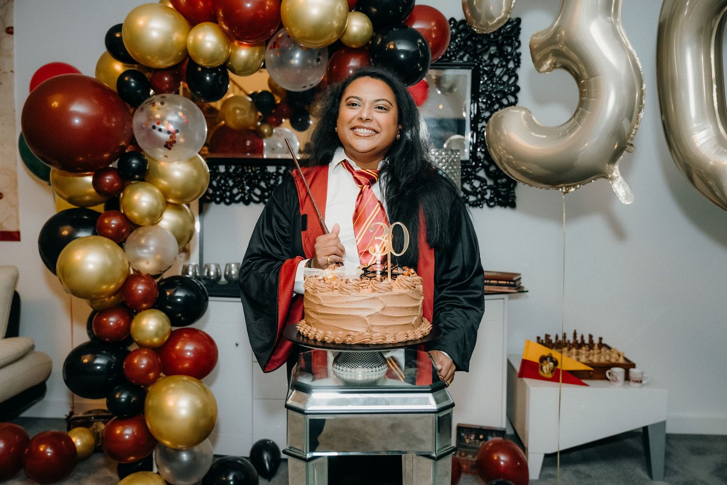 Elegant party decor featuring a luxurious balloon arch with gold and burgundy balloons arranged against a wall.