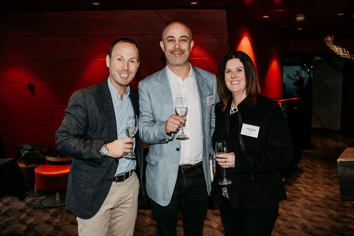 A group of people socializing and networking at an evening event with red ambient lighting.