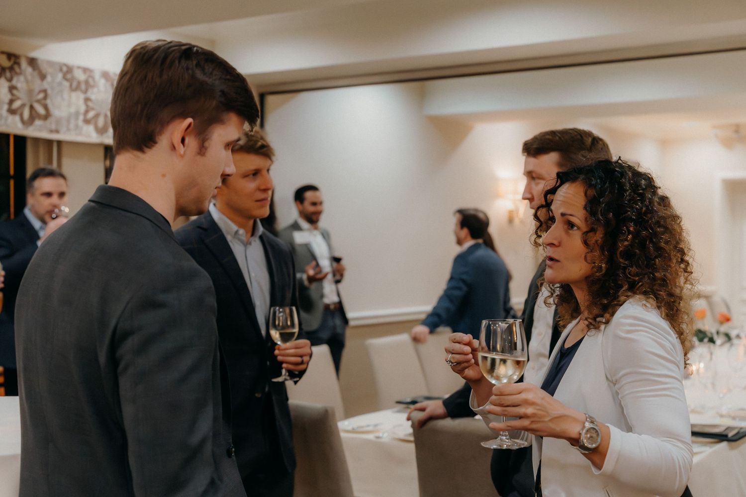 Guests mingle and socialize at an indoor event while holding drinks and engaging in conversation.
