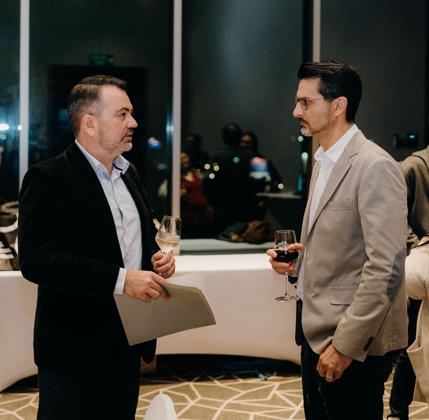 Business professionals engaged in conversation at an evening networking event in a modern office space.