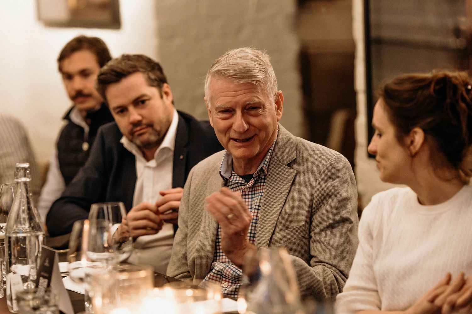 People gathered around a dining table at an upscale restaurant enjoying conversation and wine.