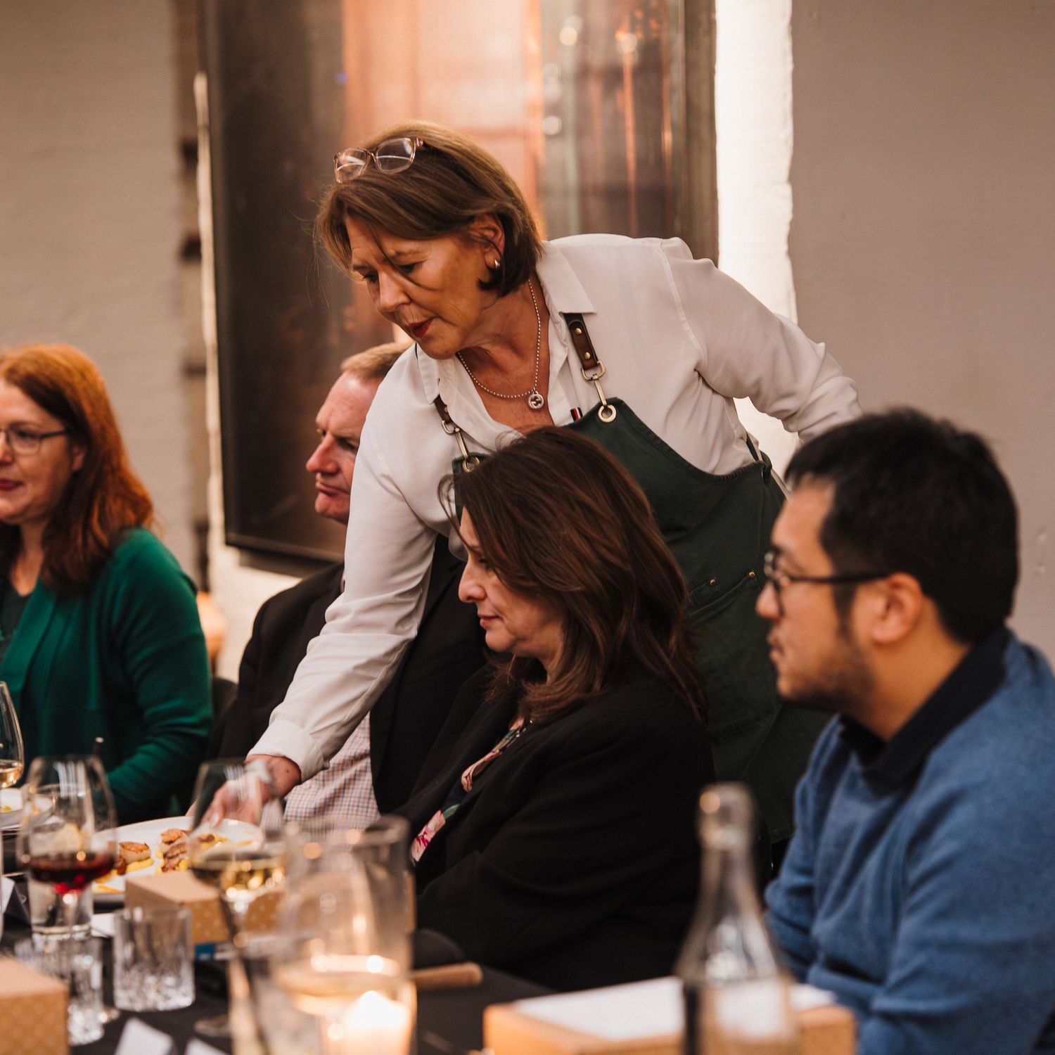 Diverse group of people engaged in conversation at a restaurant table while a server assists them.