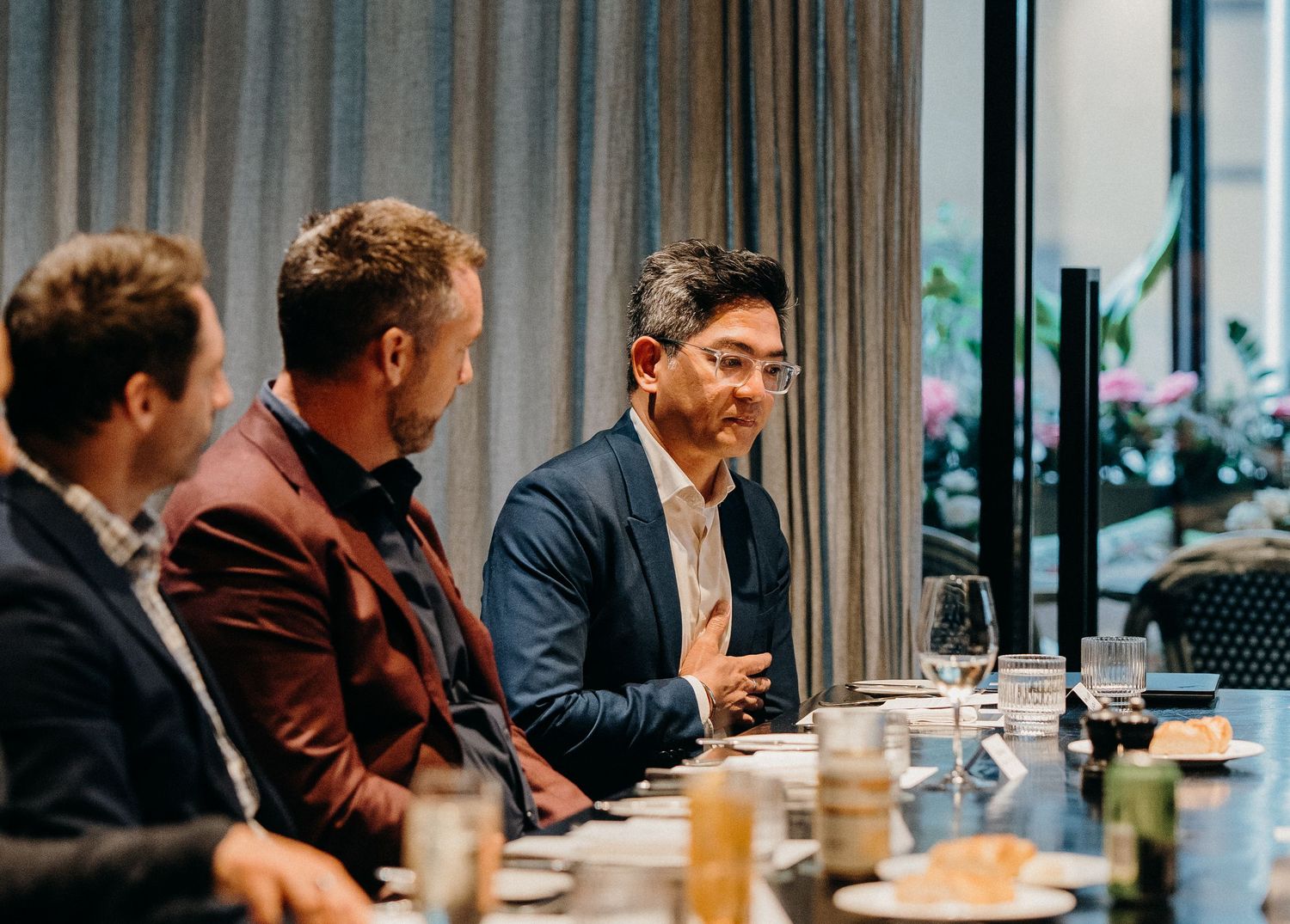 Business professionals seated at a long conference table during a corporate meeting with drinks and laptops.