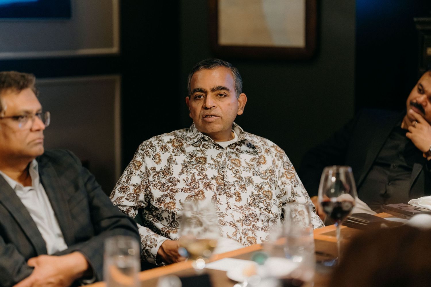 Business professionals sit around a conference table during a corporate meeting in a dimly lit room.